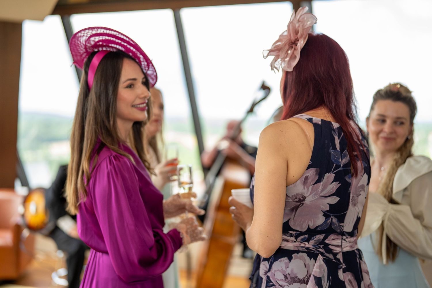 Elegantly dressed women in fascinators enjoying champagne at a sophisticated indoor garden party event.