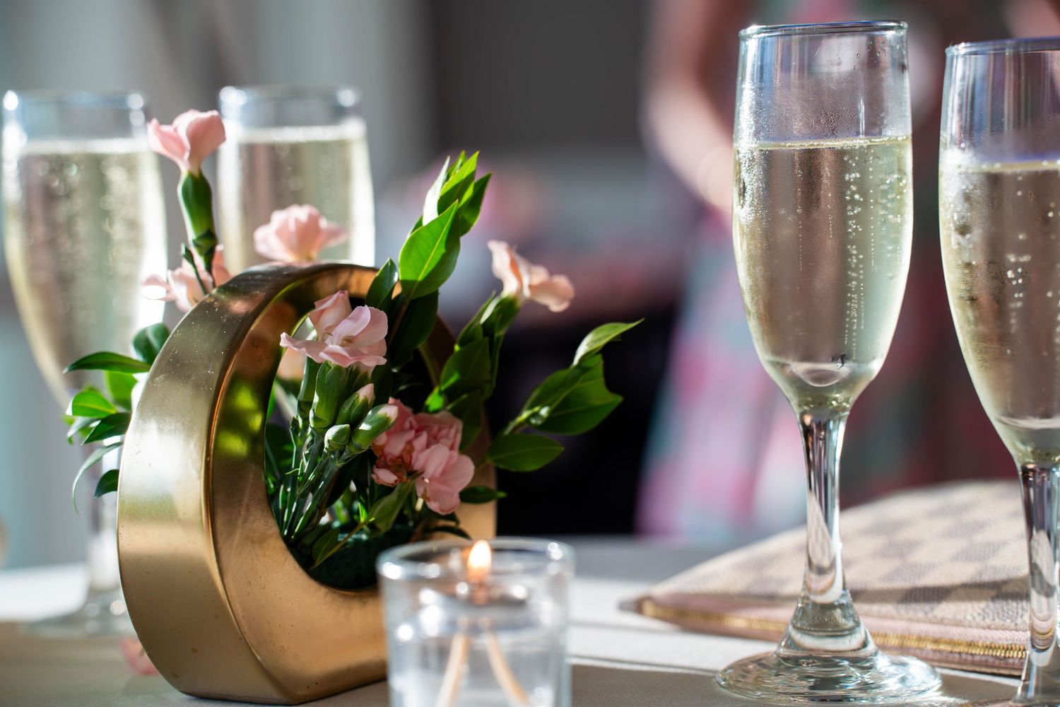 Elegant champagne flutes with pink flowers in a gold vase on a table at a celebration event.