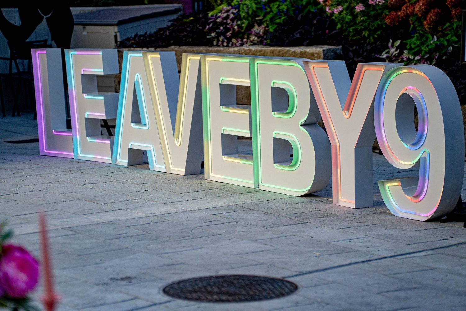 Illuminated colorful LED letter signs spelling LEAVE BY 9 displayed outdoors on a sidewalk at an evening event.