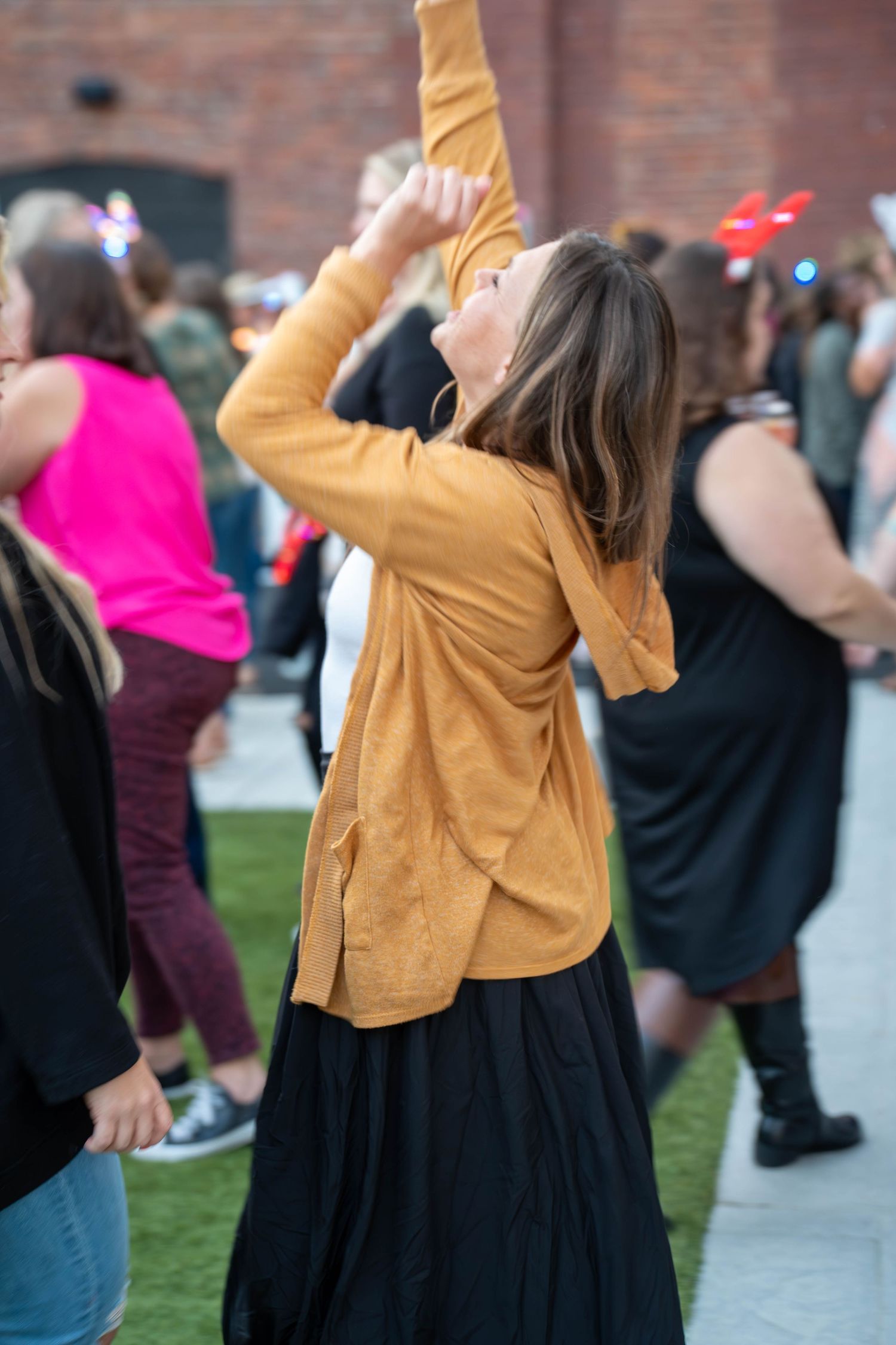 Woman in mustard yellow cardigan dancing outdoors at a social event with other guests in background.