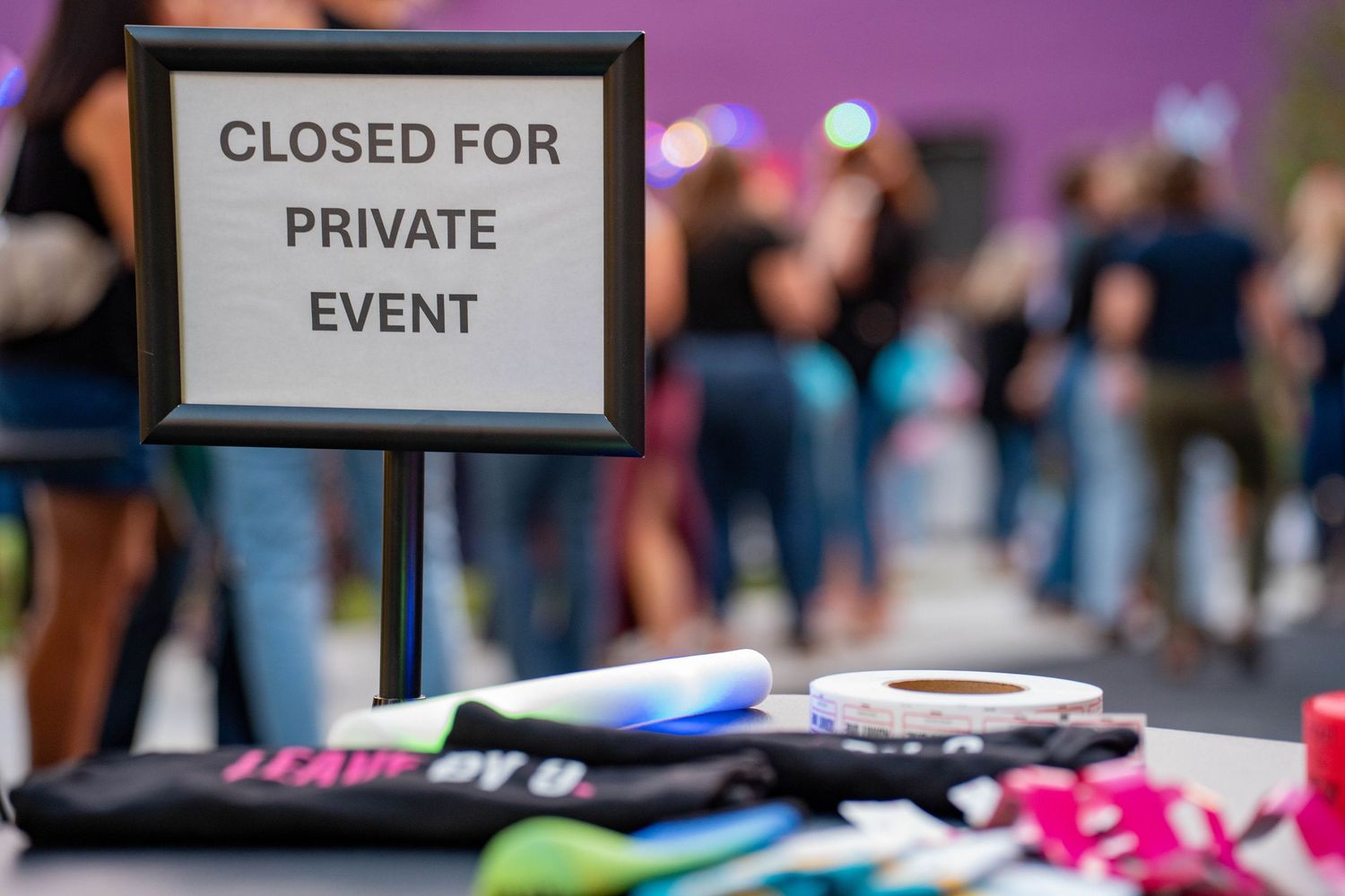 A "Closed for Private Event" sign on a table with merchandise items and blurred guests in the background.