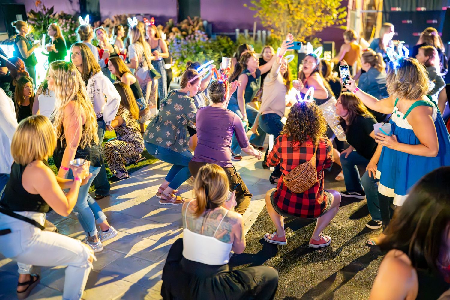 Crowd of people dancing and celebrating outdoors at a vibrant nighttime event with colorful lights.