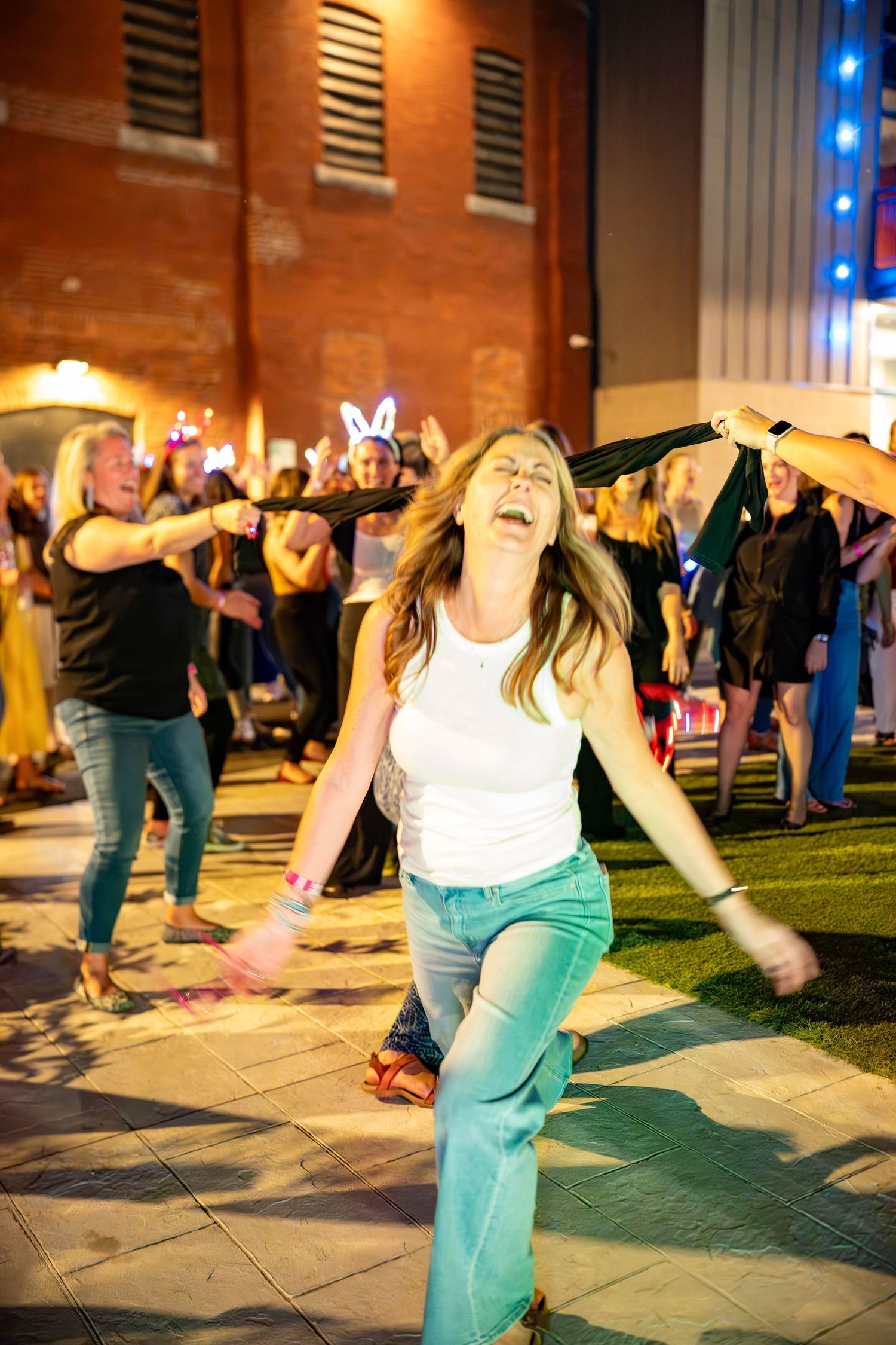 Woman in white tank top and jeans dancing joyfully outdoors at a nighttime party event.