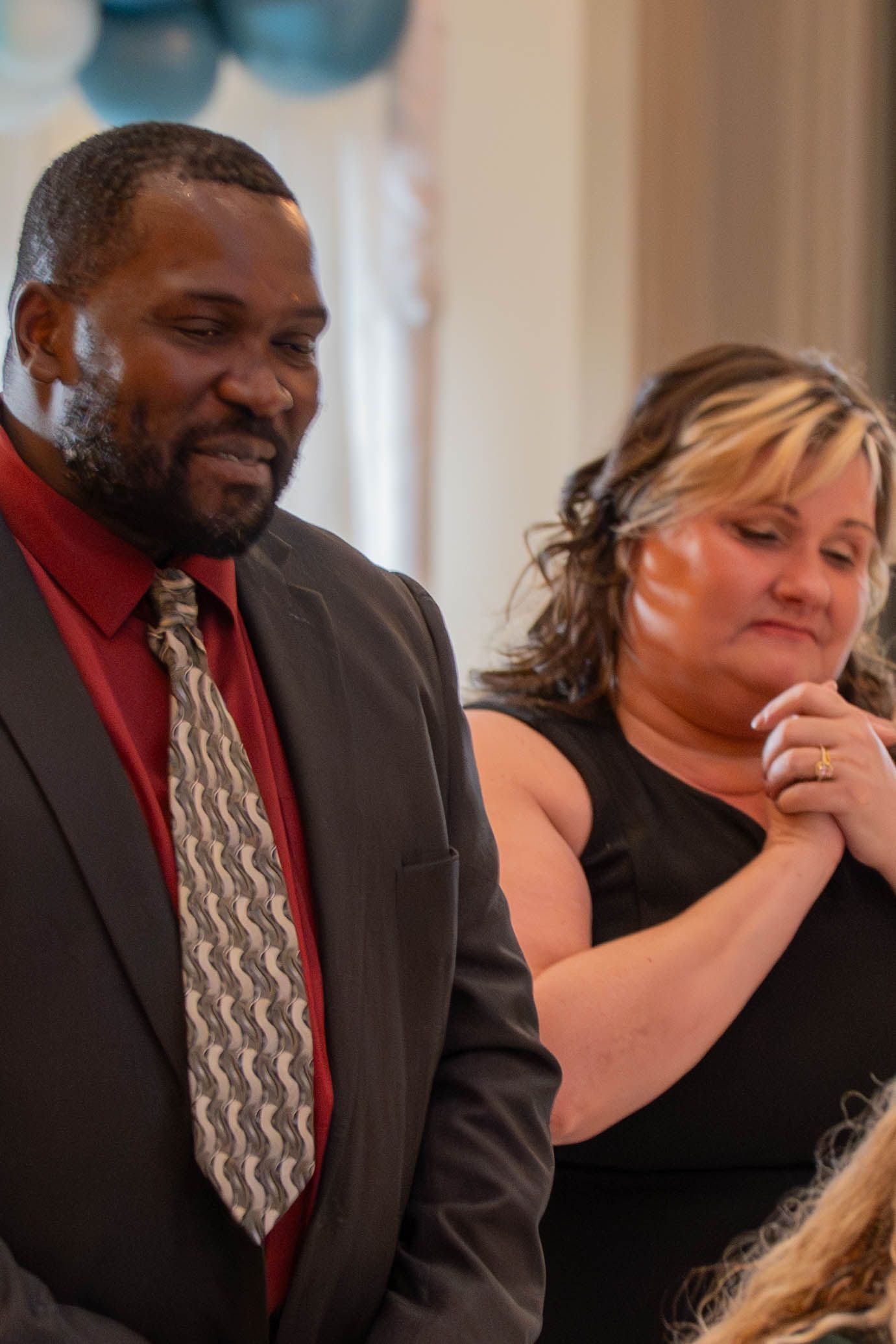 A man in a gray suit and patterned tie stands beside a woman in a black dress at a formal event.
