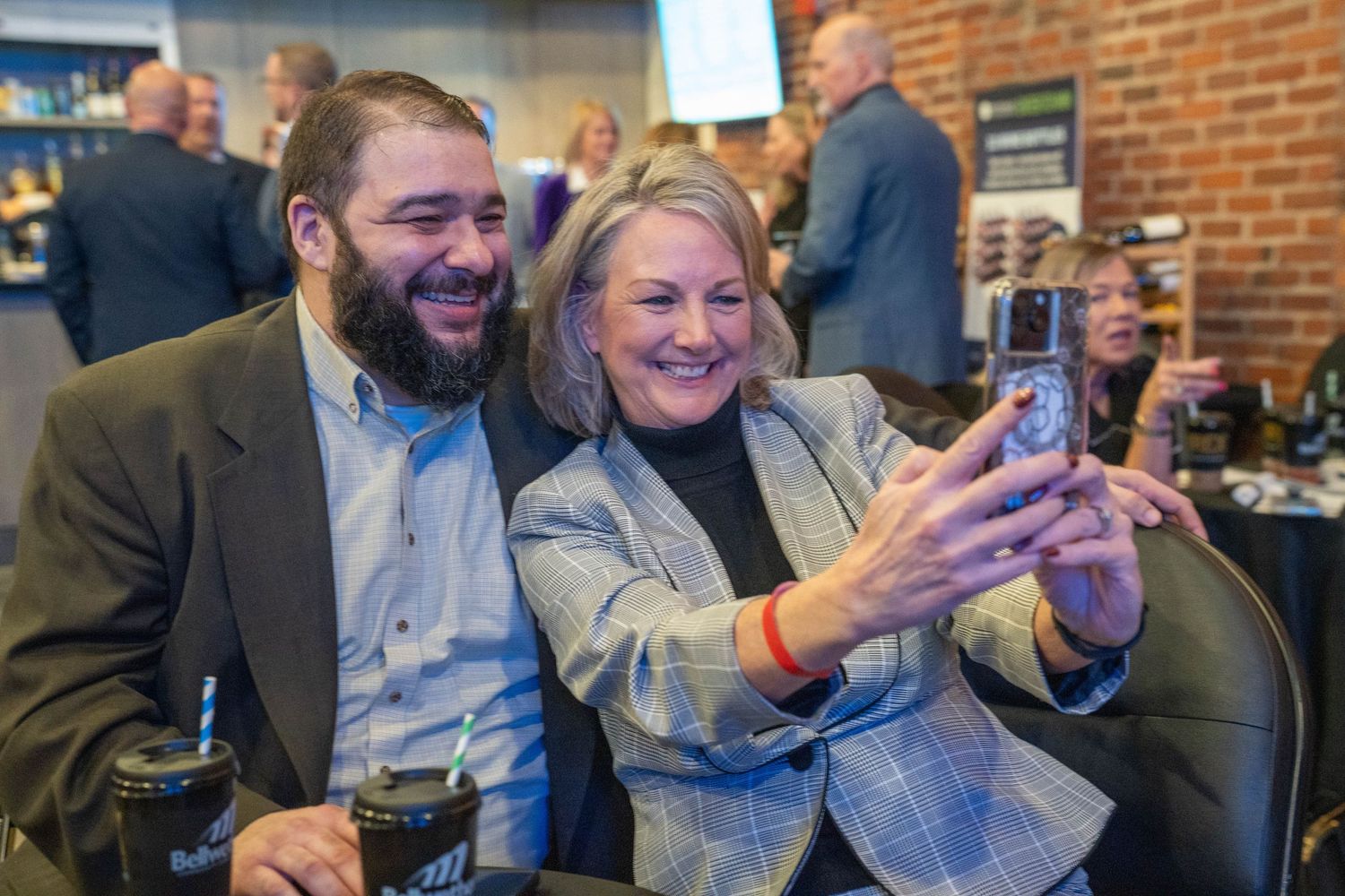 Two people smiling and taking a selfie together at a social gathering event indoors.