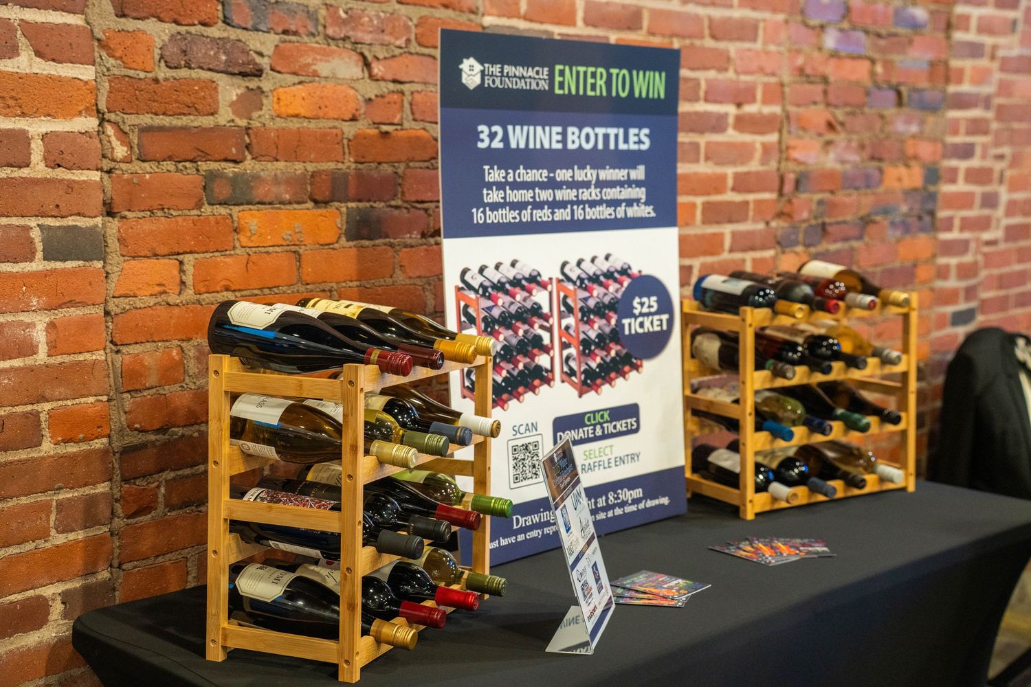 Wine bottle raffle display with 32 bottles on wooden racks beside an enter-to-win sign at an indoor event.