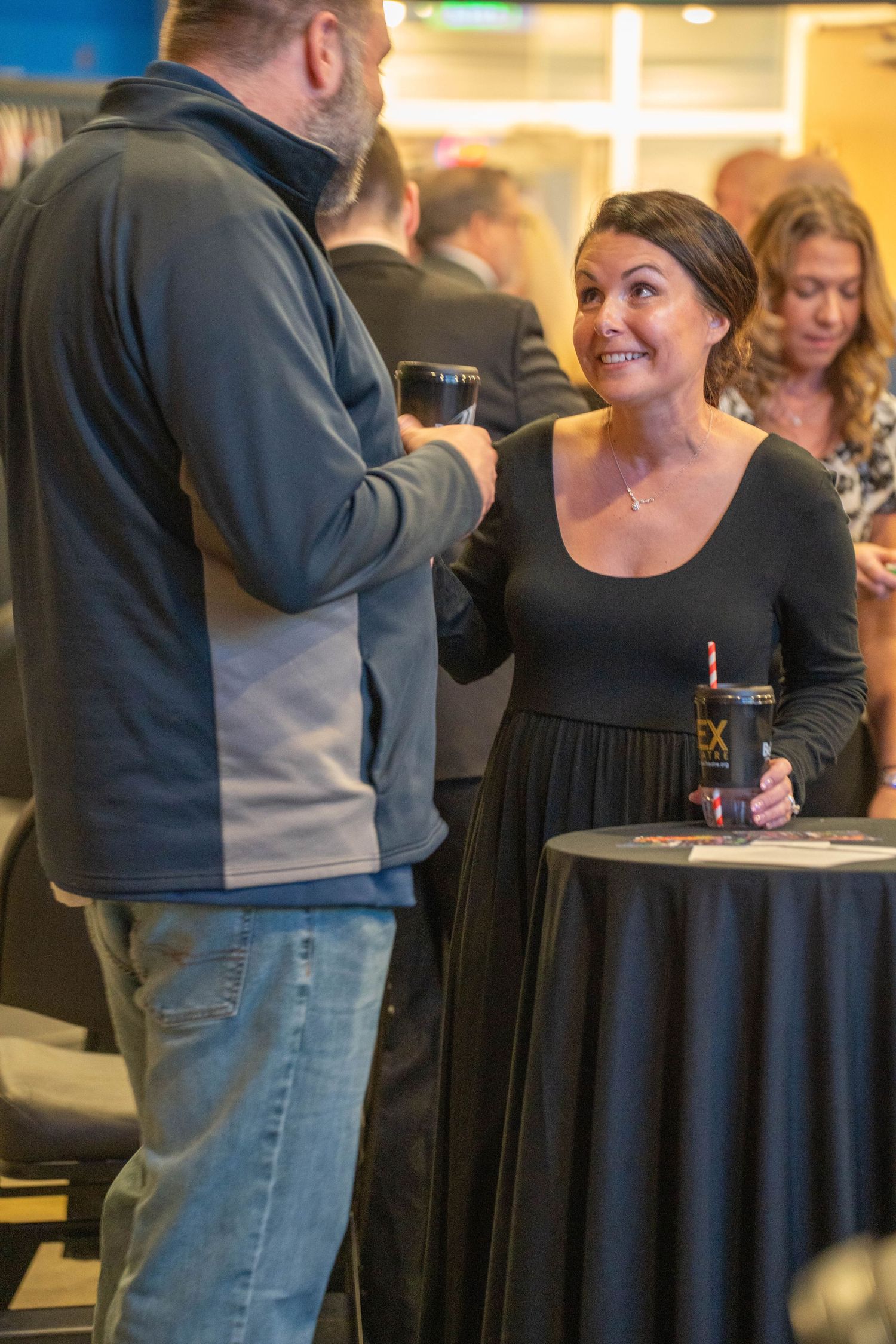 A woman in a black dress smiles while conversing with a man at a social networking event.