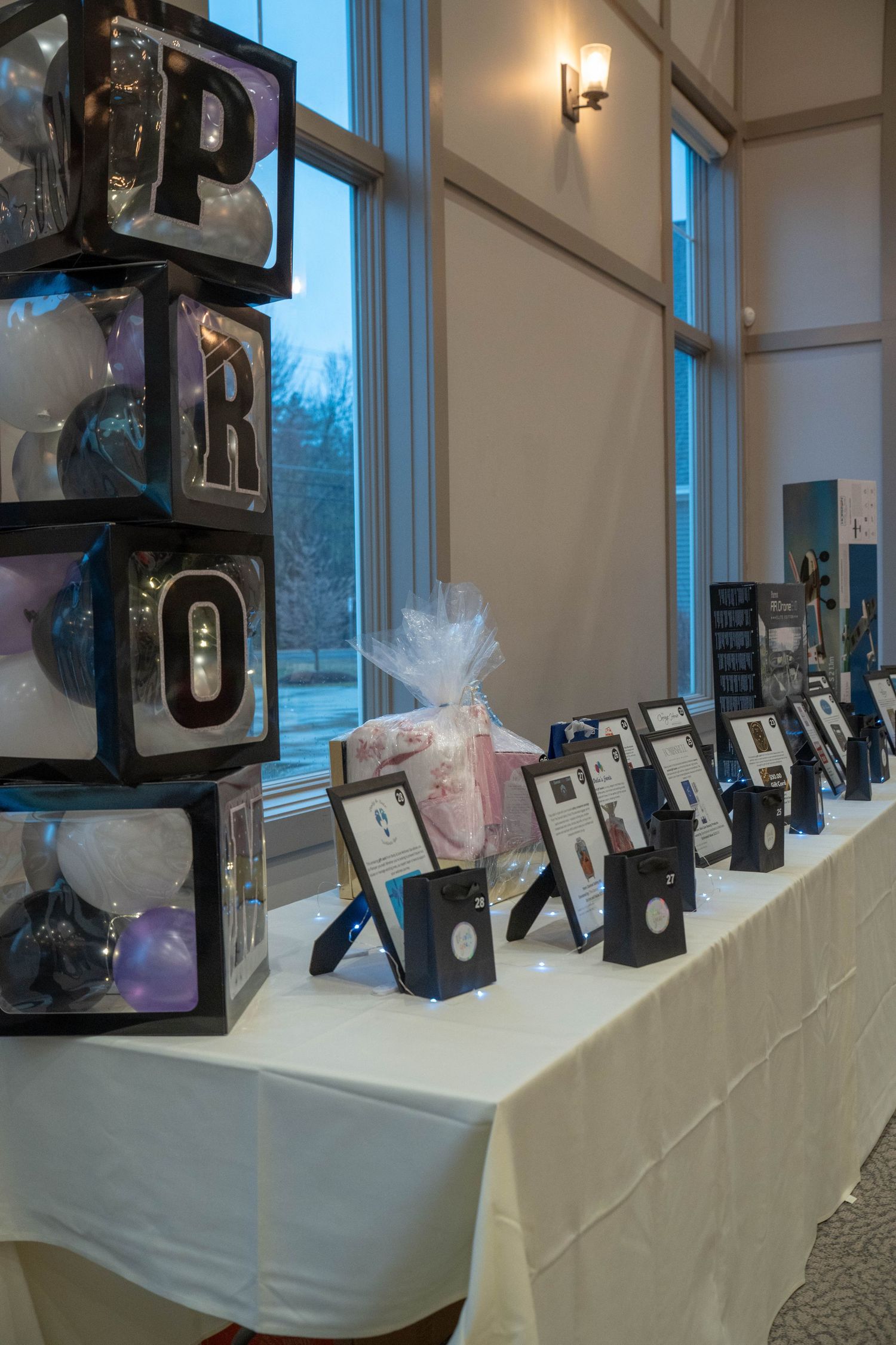 Prom decoration table with balloon letter boxes, framed photos, and gift displays in an elegant event venue.