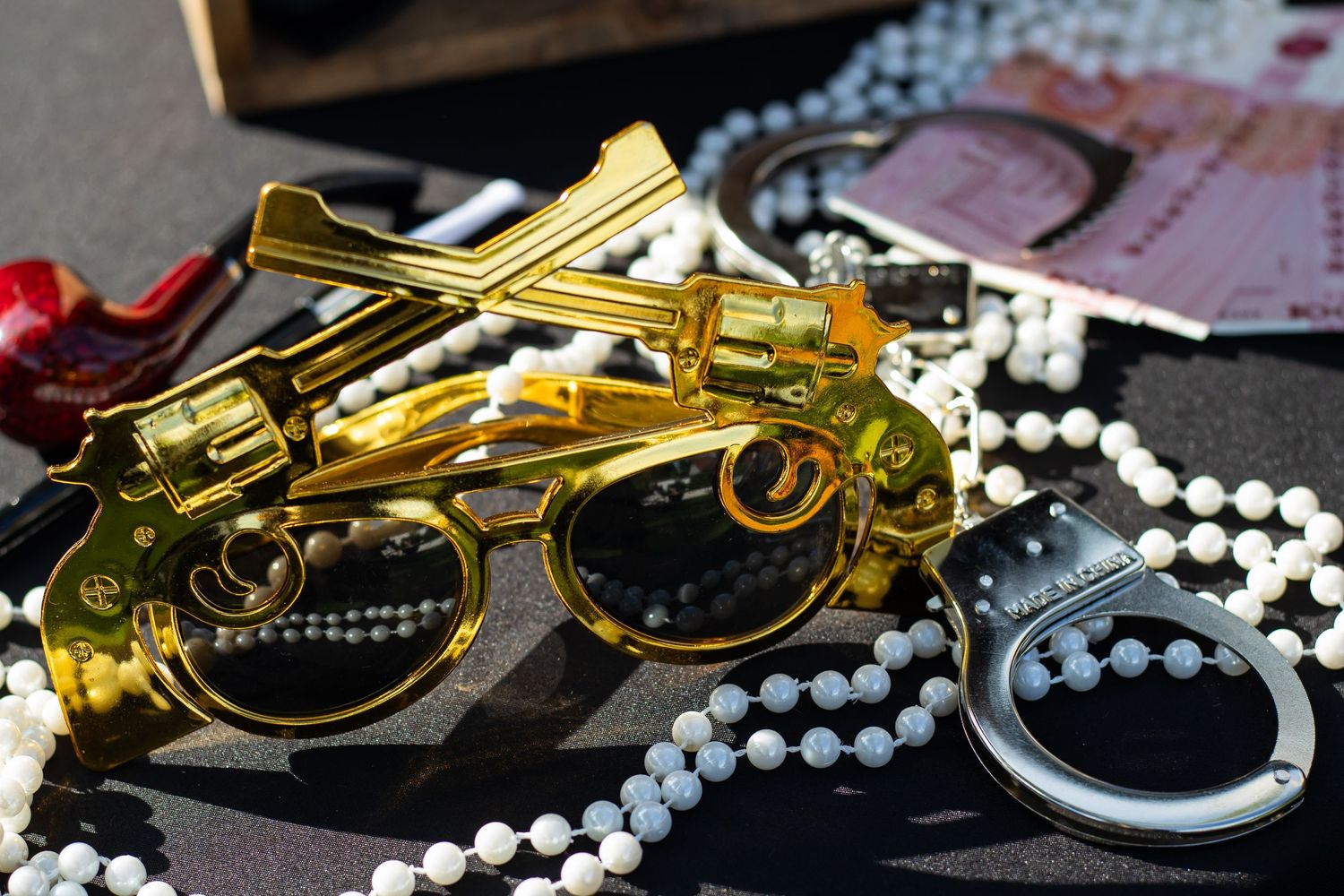 Gold toy guns, pearl beads, handcuffs, and sunglasses arranged on a dark surface as costume accessories.