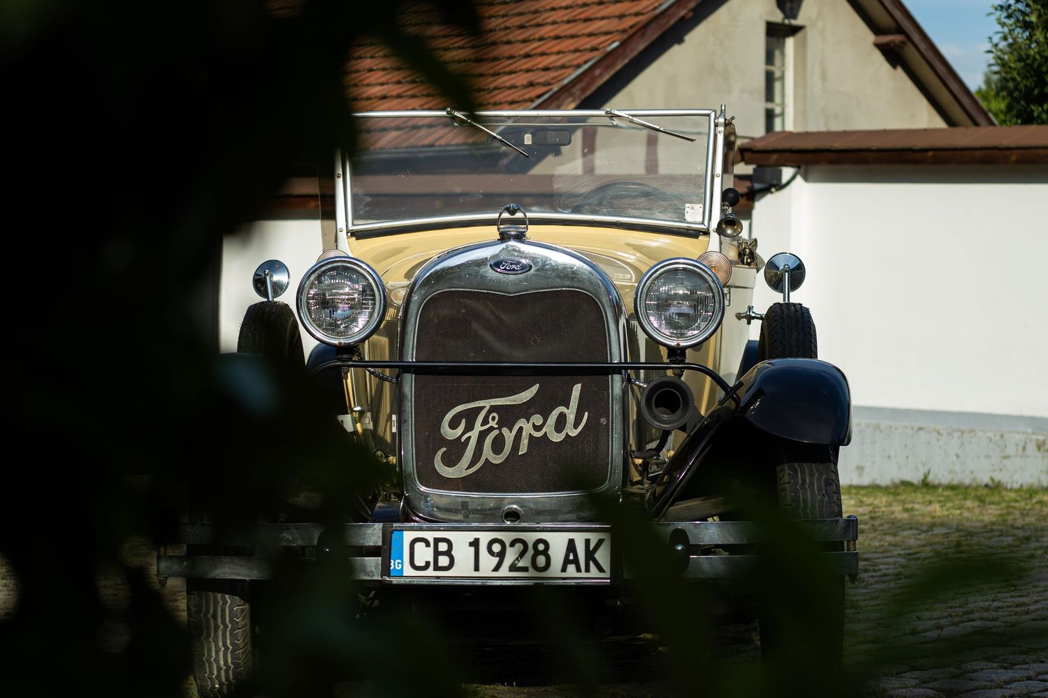 Vintage Ford car from 1928 with license plate CB 1928 AK parked in front of a white building.