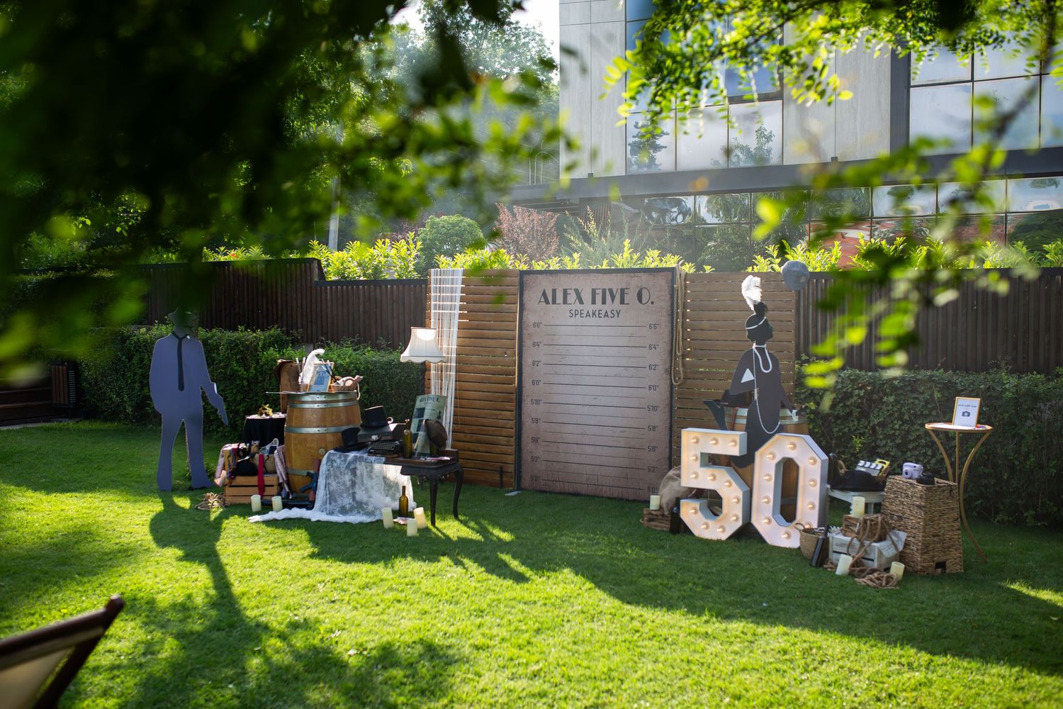 Outdoor 50th birthday party setup with suit display, wooden barrel, and large number 50 sign on green lawn.