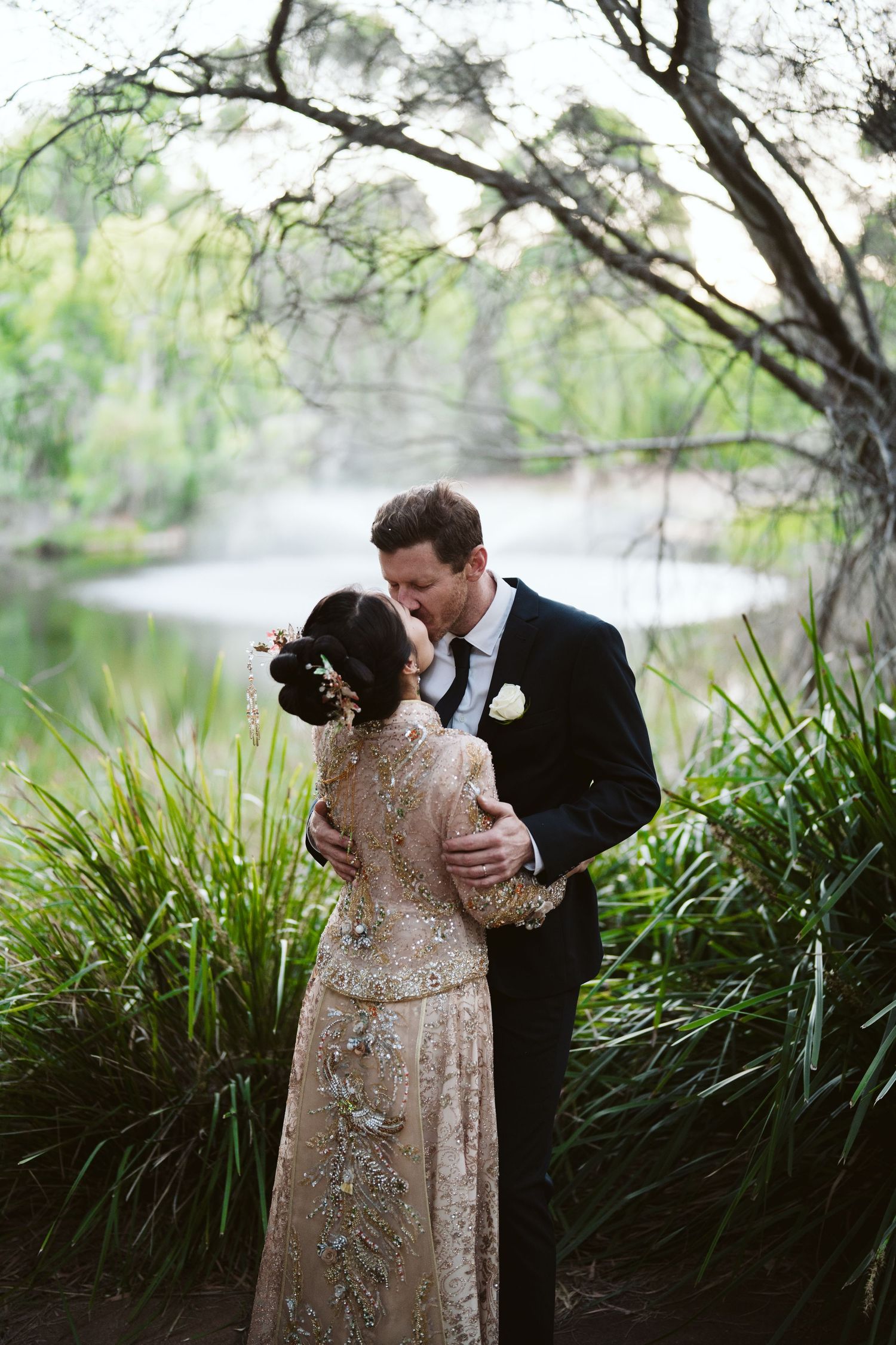 Cameron and Lulu standing together by the lake under the trees
