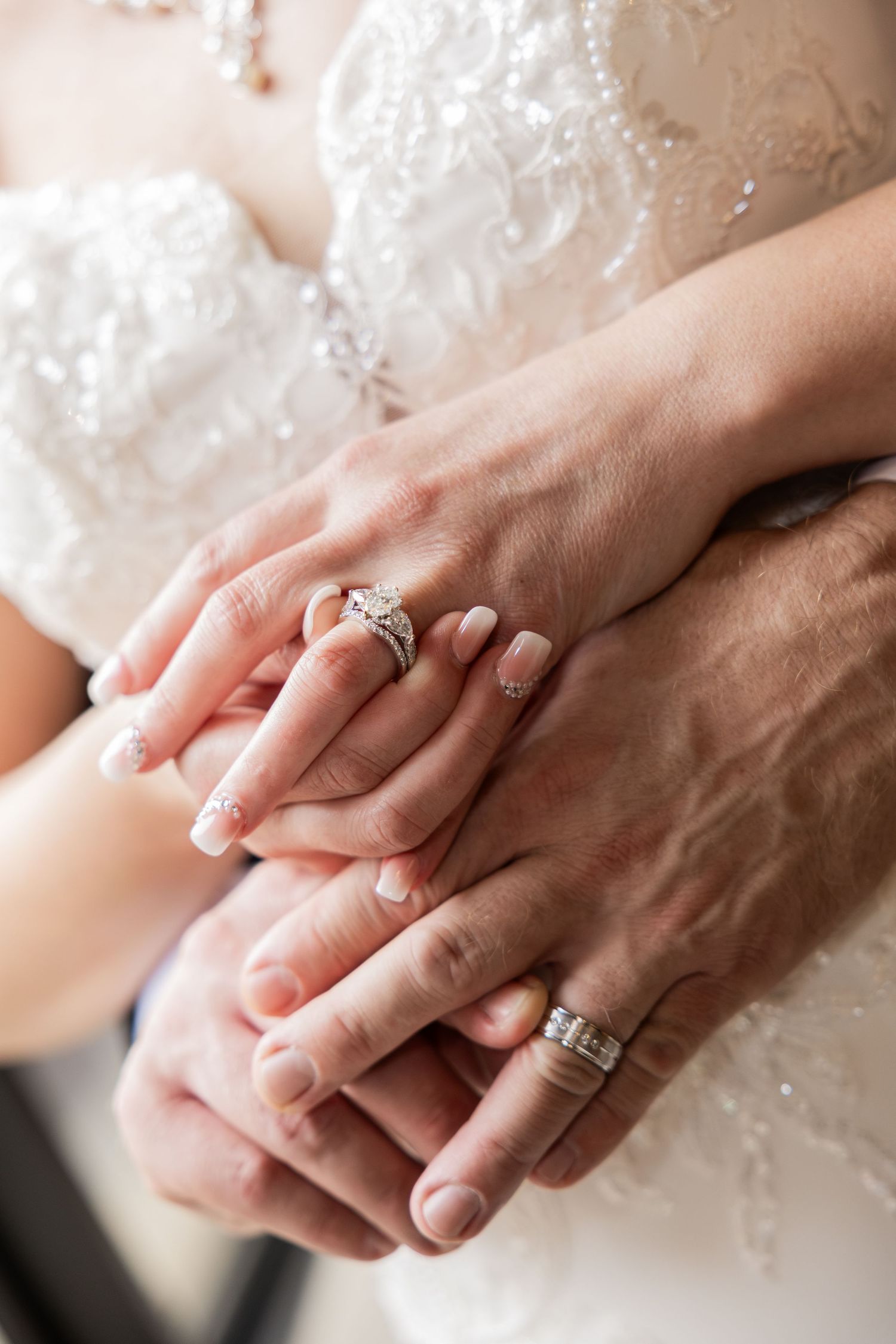 Bride and groom holding hands showing wedding rings, bride wearing diamond engagement ring and white lace gown.