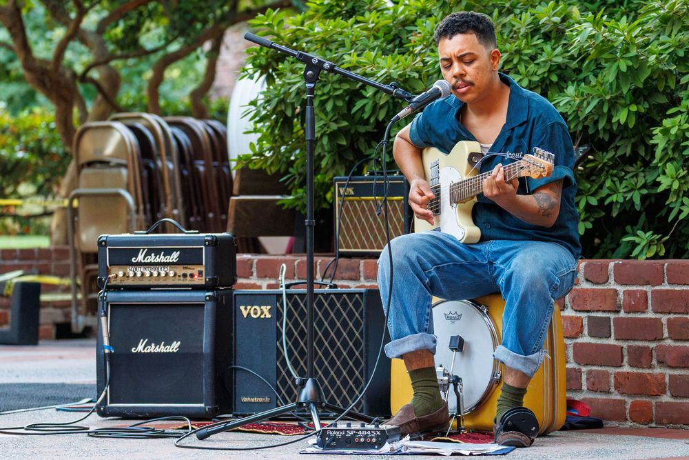 Musician playing electric guitar outdoors with Marshall and VOX amplifiers at a street performance.