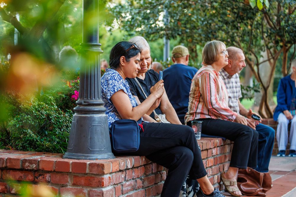 People sitting on a brick wall in a garden, socializing and smiling outdoors near a lamppost.