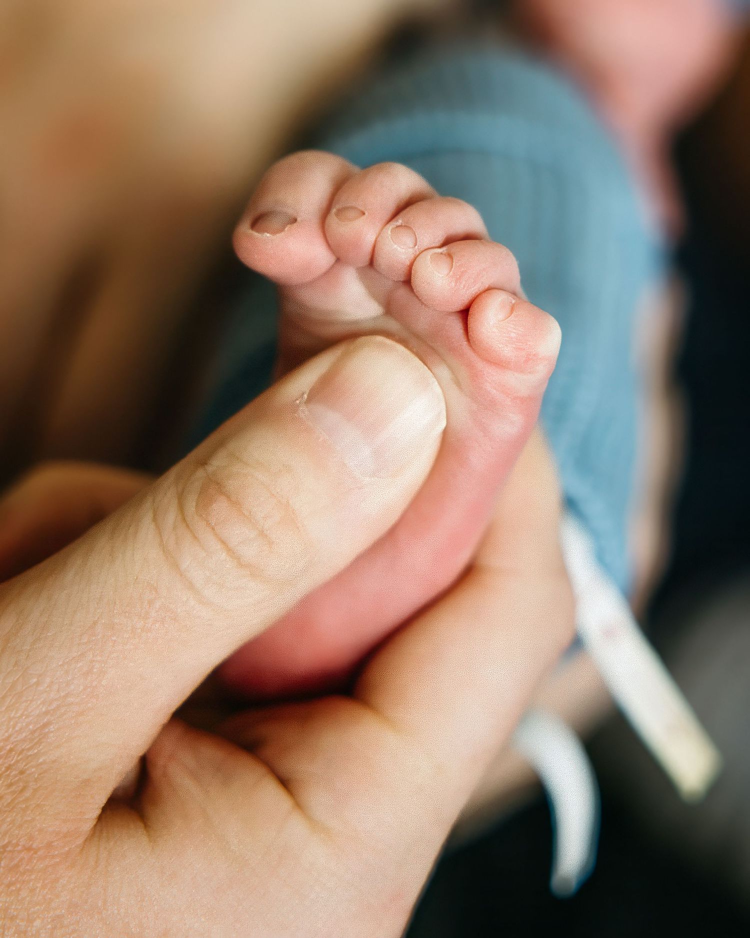 Close-up of an adult finger gently holding a newborn baby's tiny foot, showcasing delicate toes and soft skin.