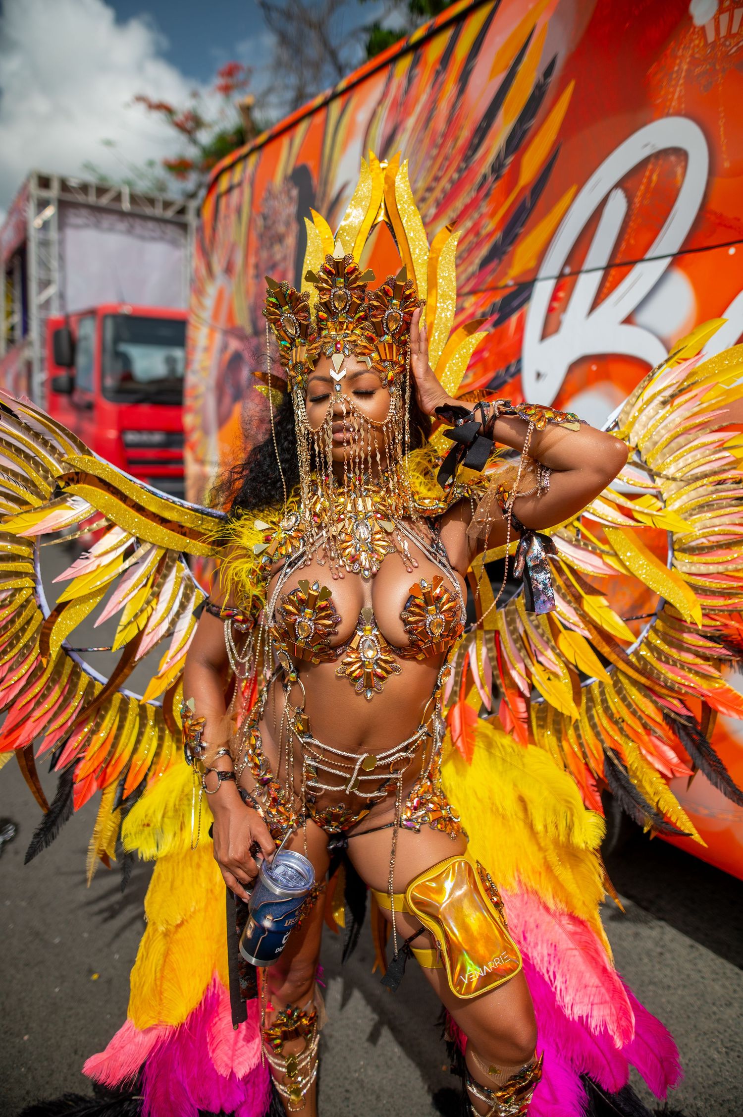 Woman in colorful beaded carnival costume with headdress posing outdoors on green grass.