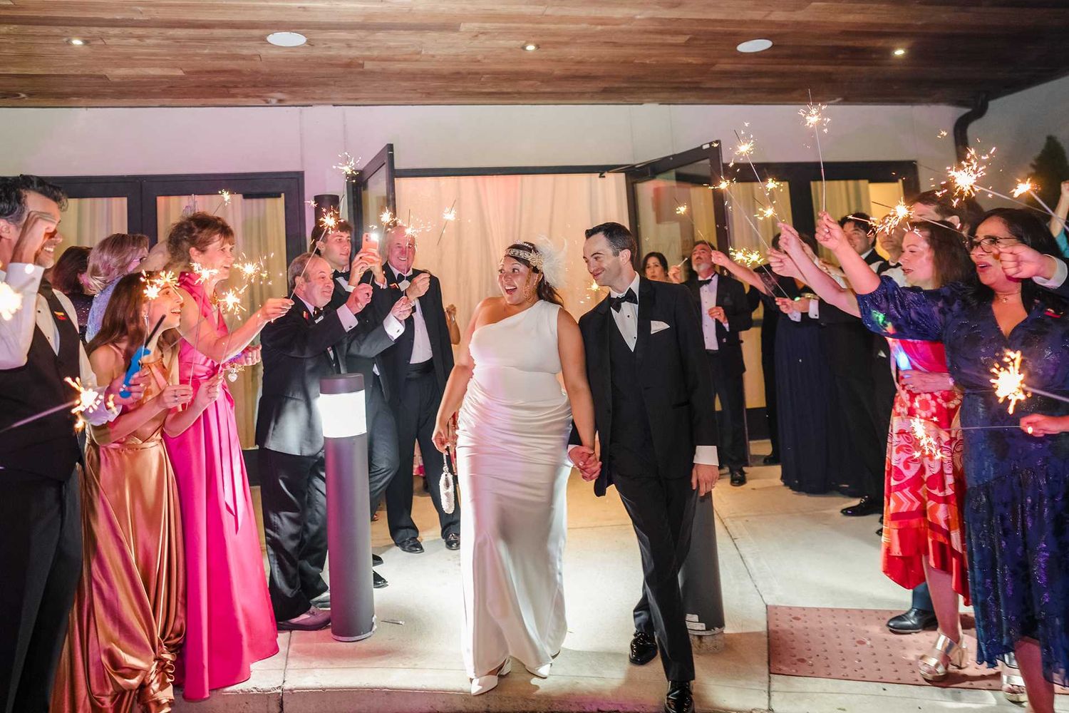 Bride and groom exit wedding reception through sparkler tunnel surrounded by guests in formal attire at the view wedding venue