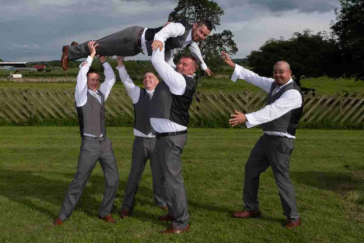 Liams groomsmen tossing him into the air outdoors at Greenhill Hotel near Wigton Cumbria