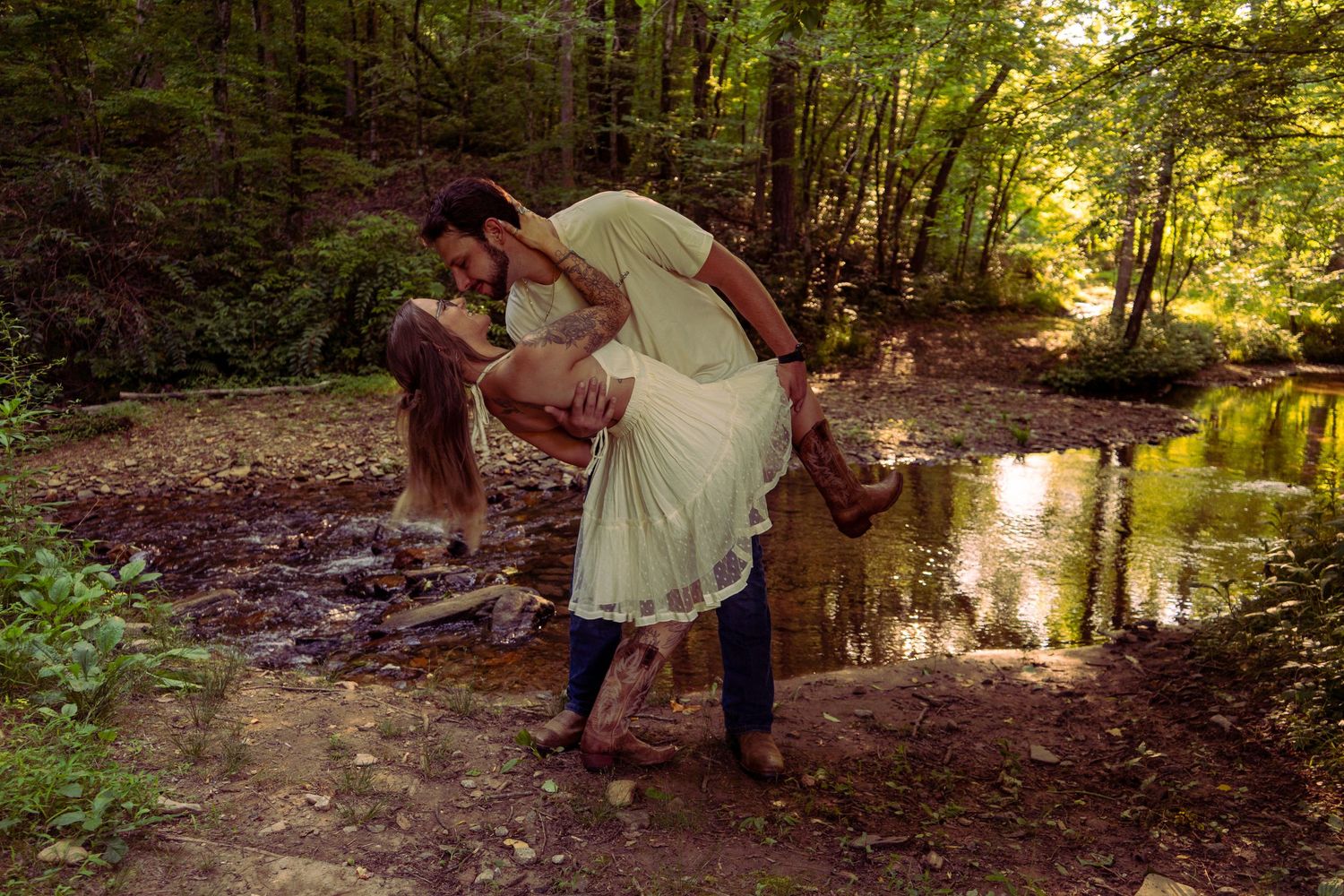 Couple sharing a romantic dip near a forest creek, man in blue jeans dipping woman in flowing green dress.