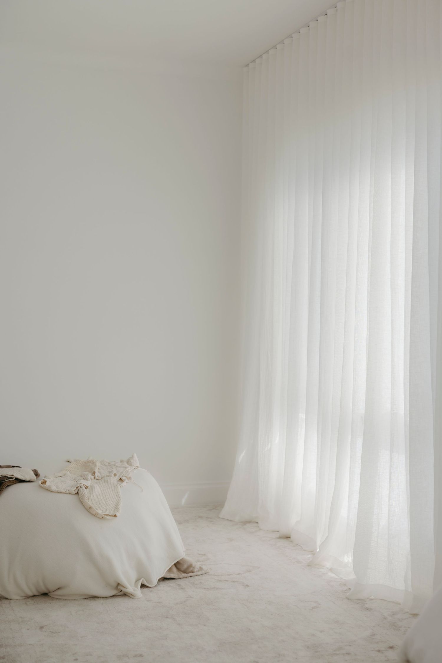 Minimalist white bedroom corner with sheer curtains, white bedding, and soft natural light creating a serene atmosphere.