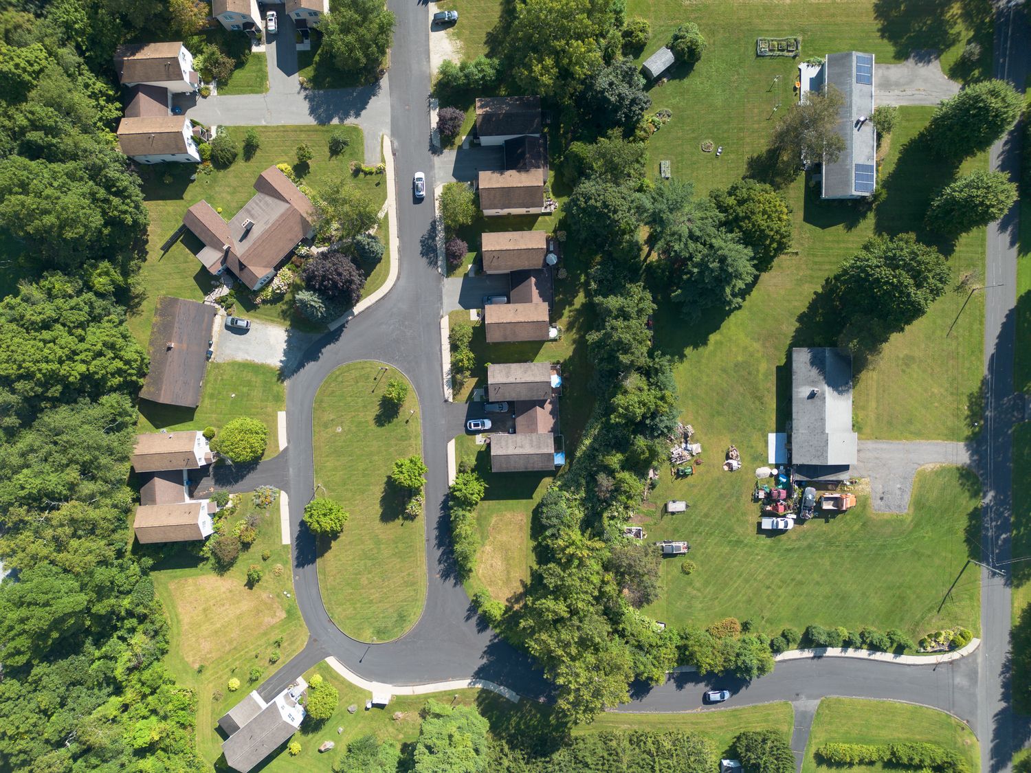 Aerial view of a quiet residential neighborhood with winding roads, green lawns, and tree-lined streets on a sunny day.