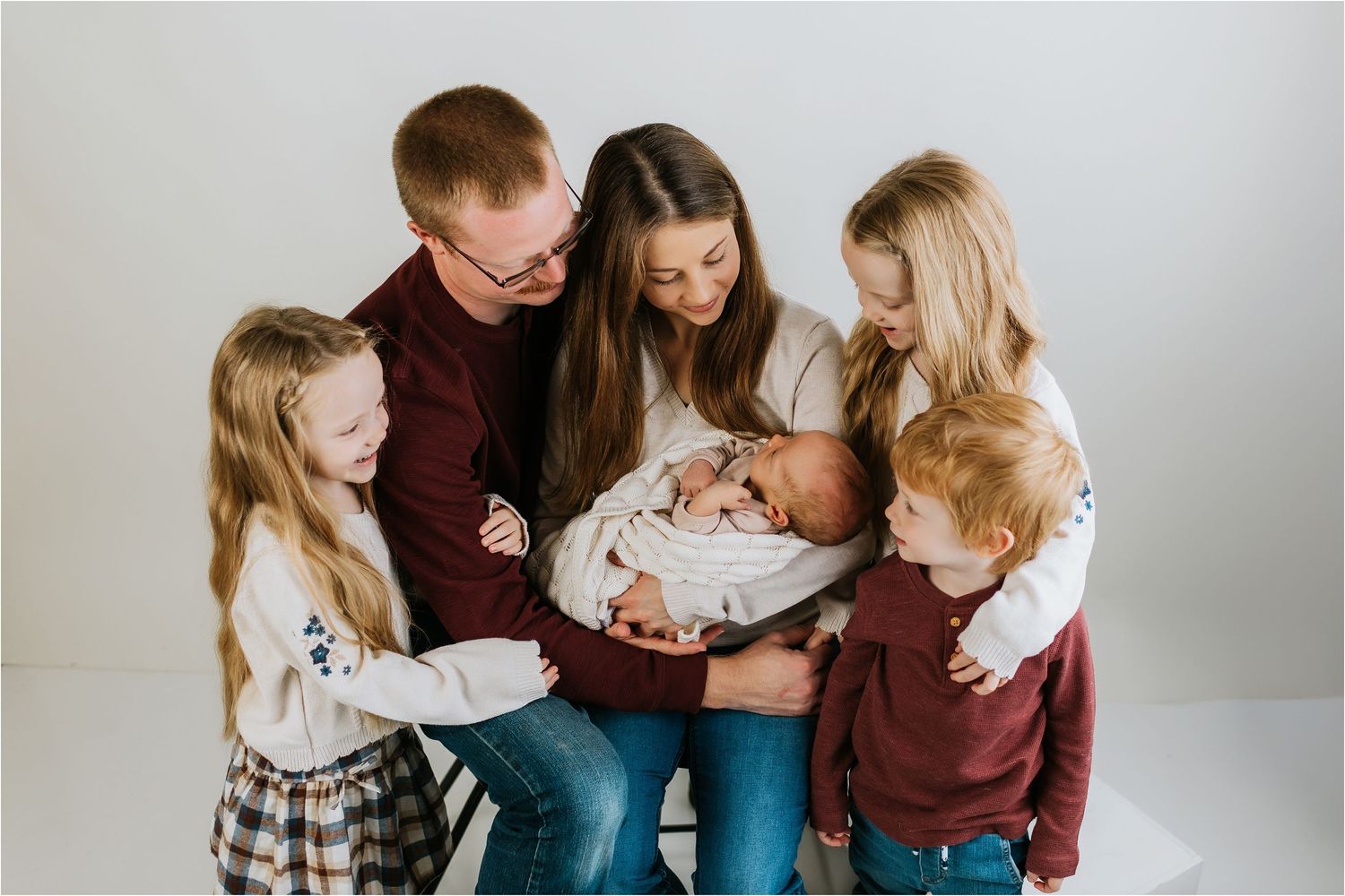 Family of six admiring their newborn baby in a bright studio portrait session.