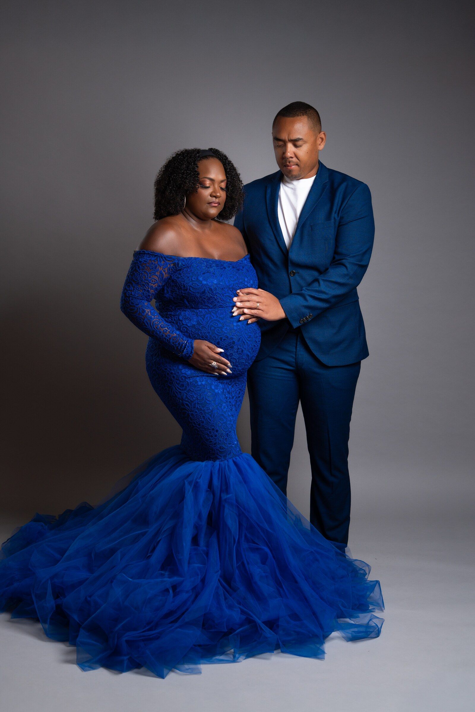 Pregnant couple in matching royal blue outfits posing elegantly in a studio maternity photoshoot.