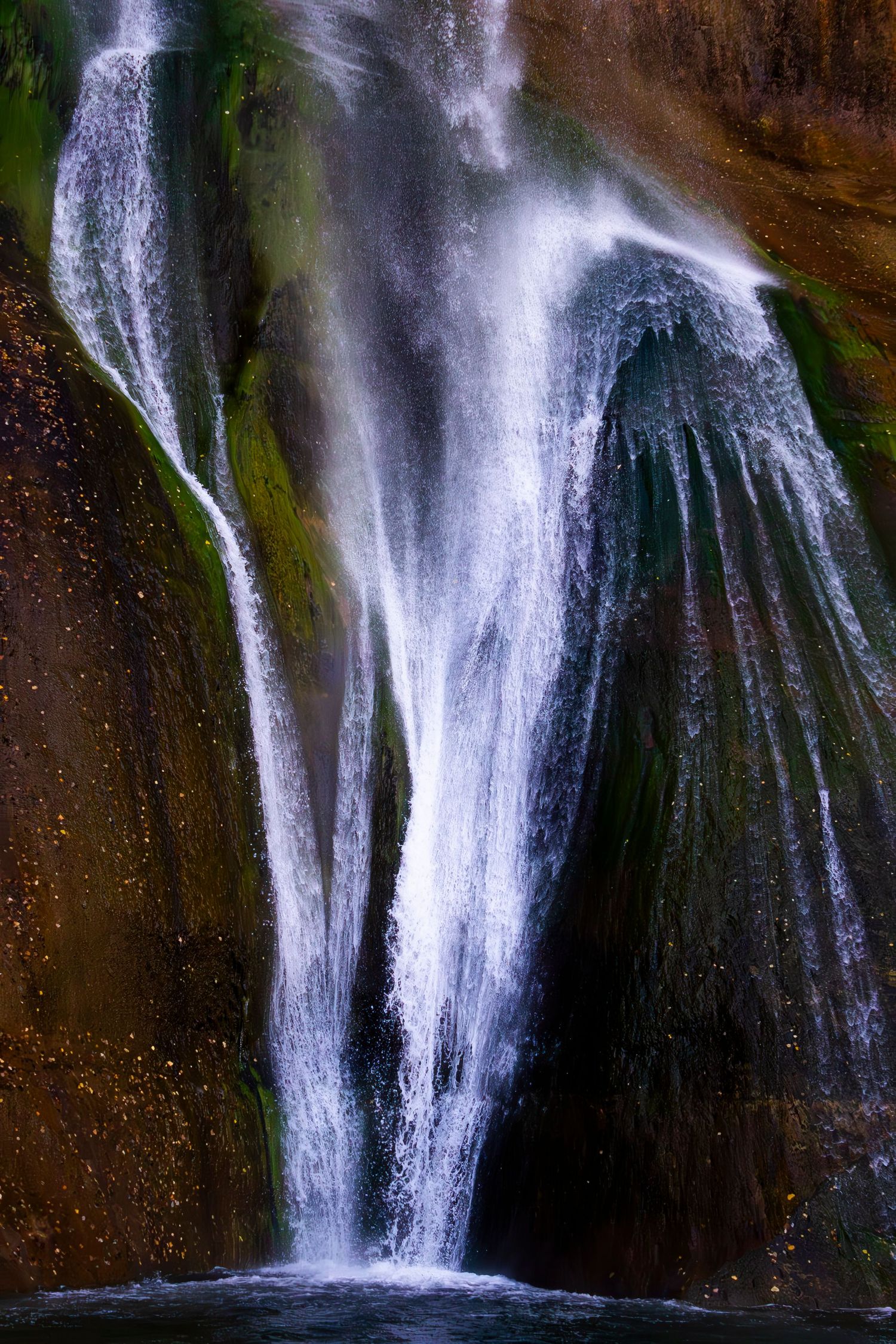A stunning waterfall cascades over moss-covered rocks, creating elegant white streams against dark stone surfaces.