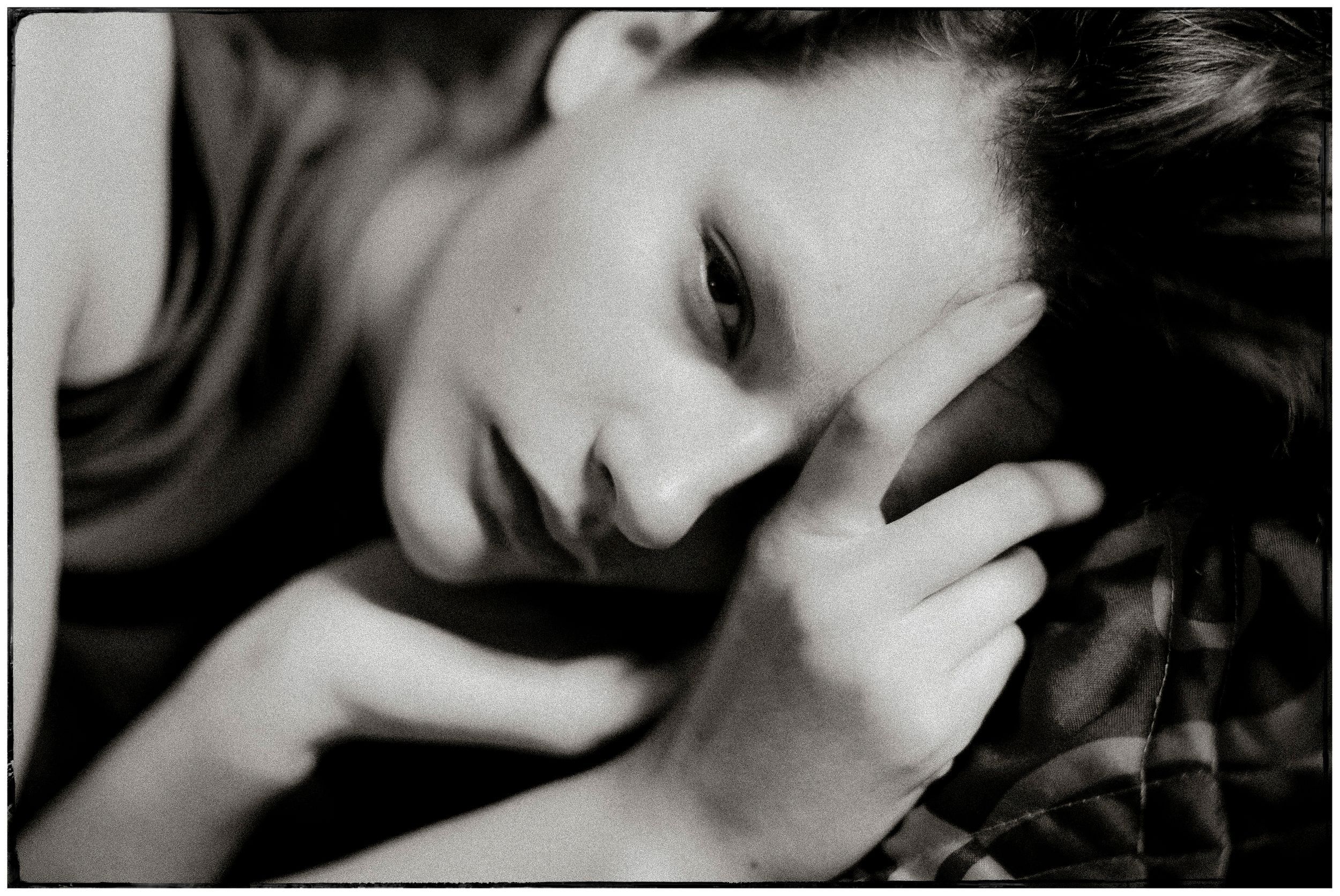 Black and white portrait of a young woman resting her head on her hand, looking pensive and contemplative.
