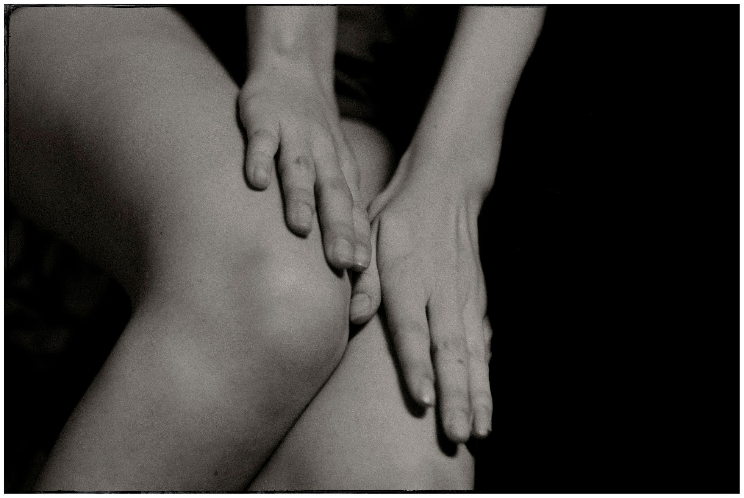 Close-up black and white photo of hands resting on bare knees in a contemplative pose.