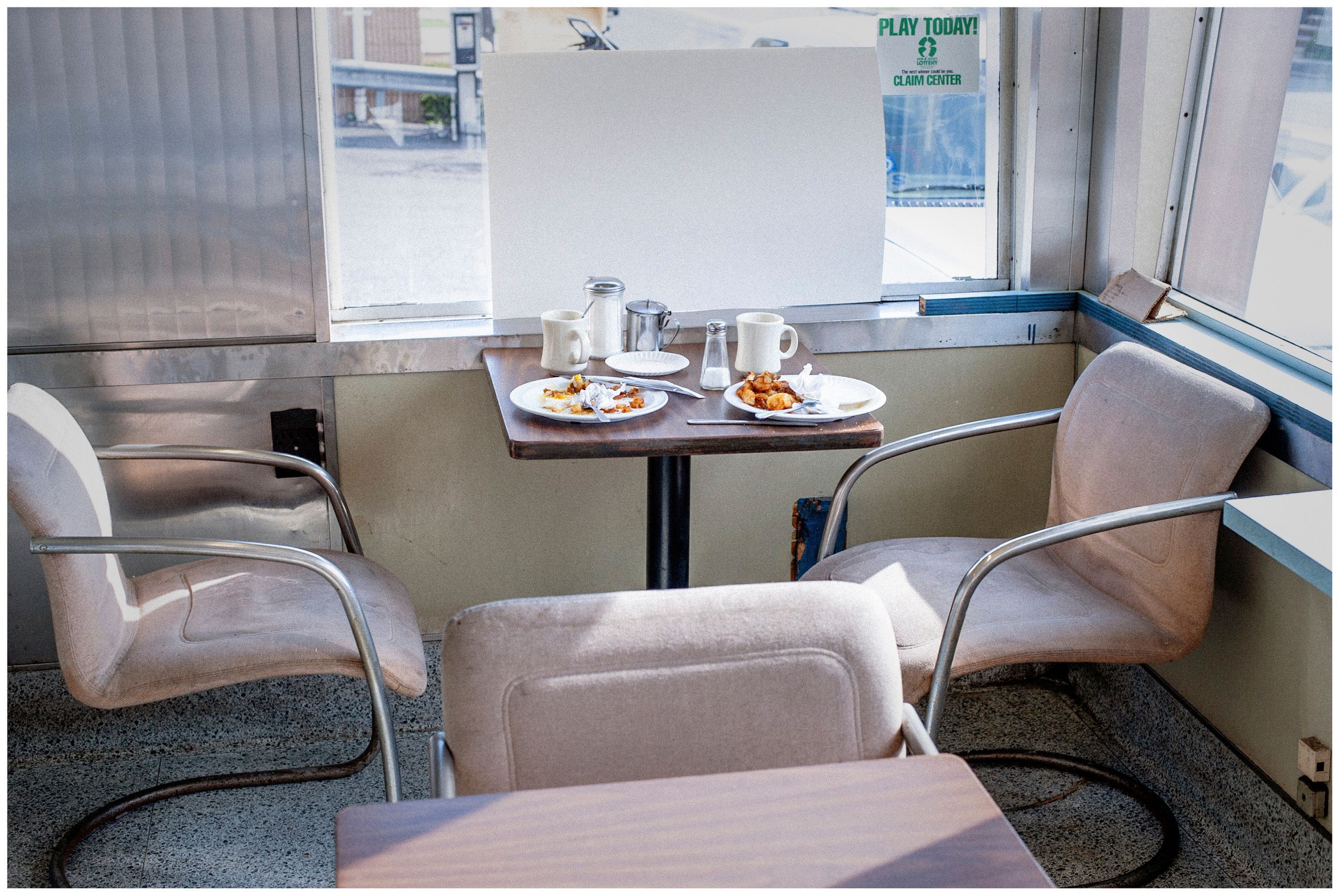 Cozy diner booth with two cushioned chairs at a small table set with plates and glasses by a window.