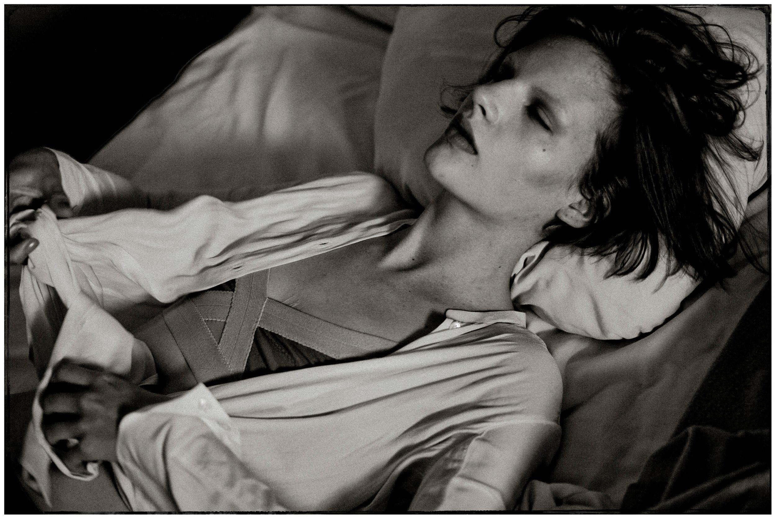 Black and white photo of a person reclining, wearing an open white shirt, with dramatic lighting and artistic composition.