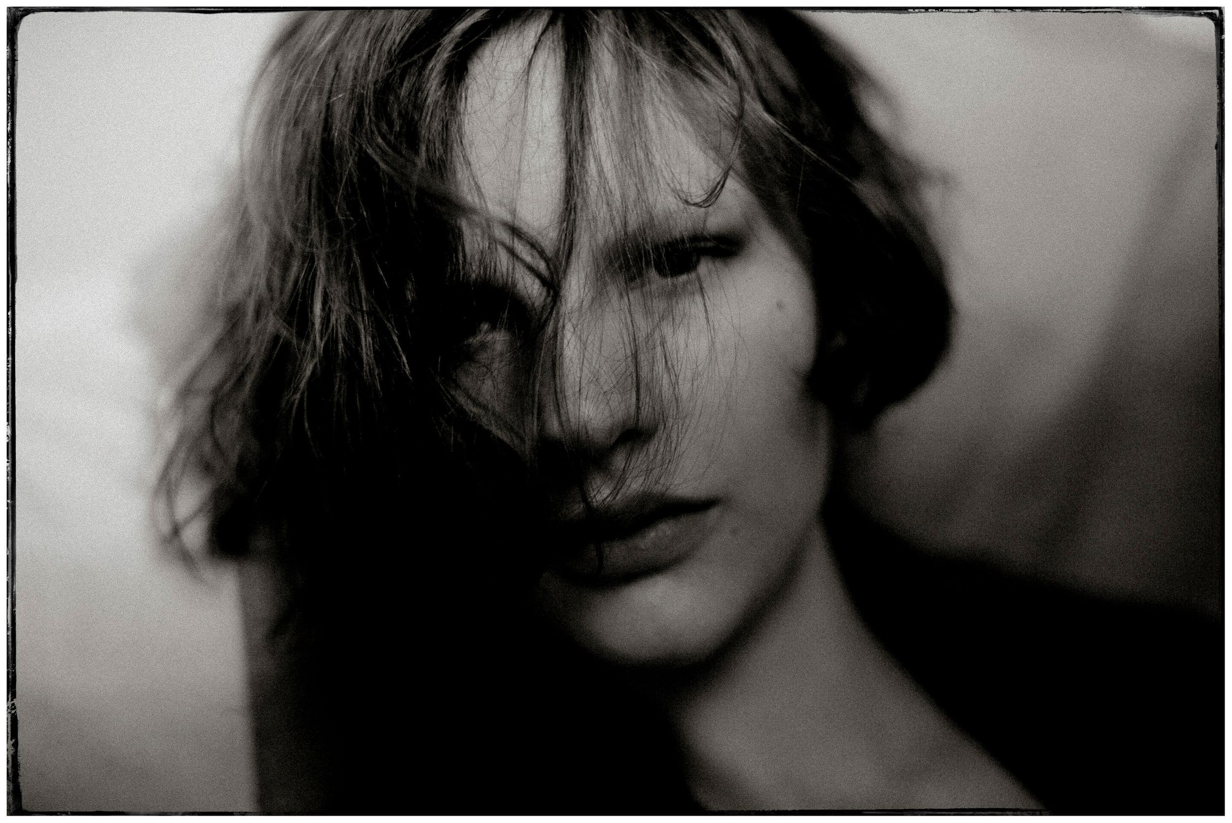 Black and white portrait of a young woman with hair covering her face, dramatic shadows, moody artistic photography.