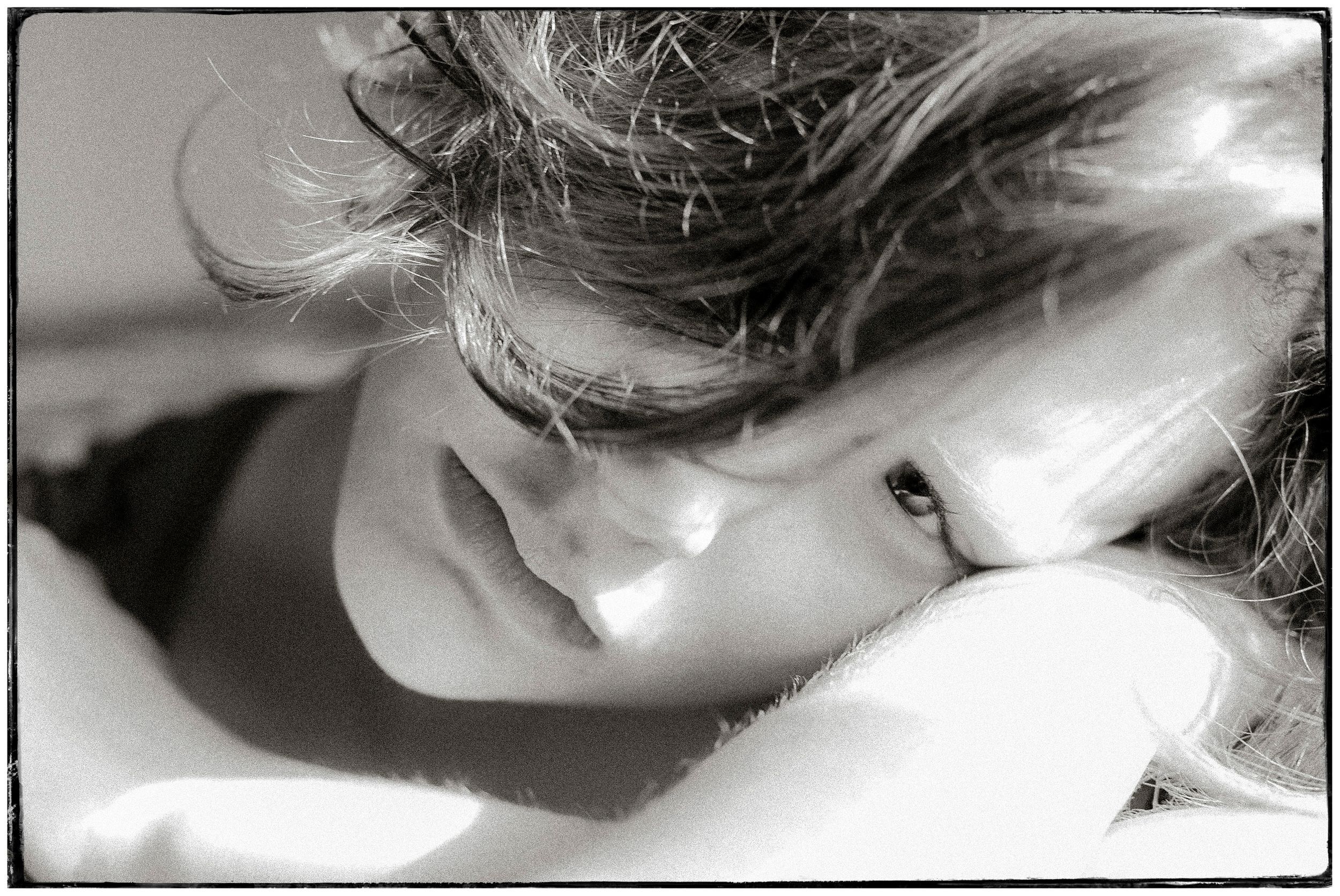 Black and white close-up portrait of a woman resting her head on her arm in soft light.