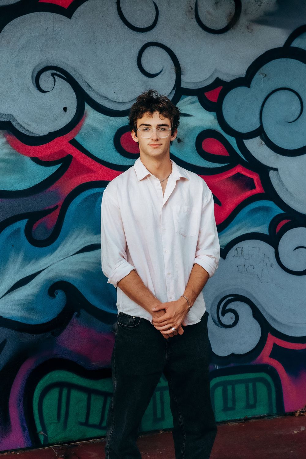 Young man in white shirt stands confidently before colorful graffiti wall art backdrop.