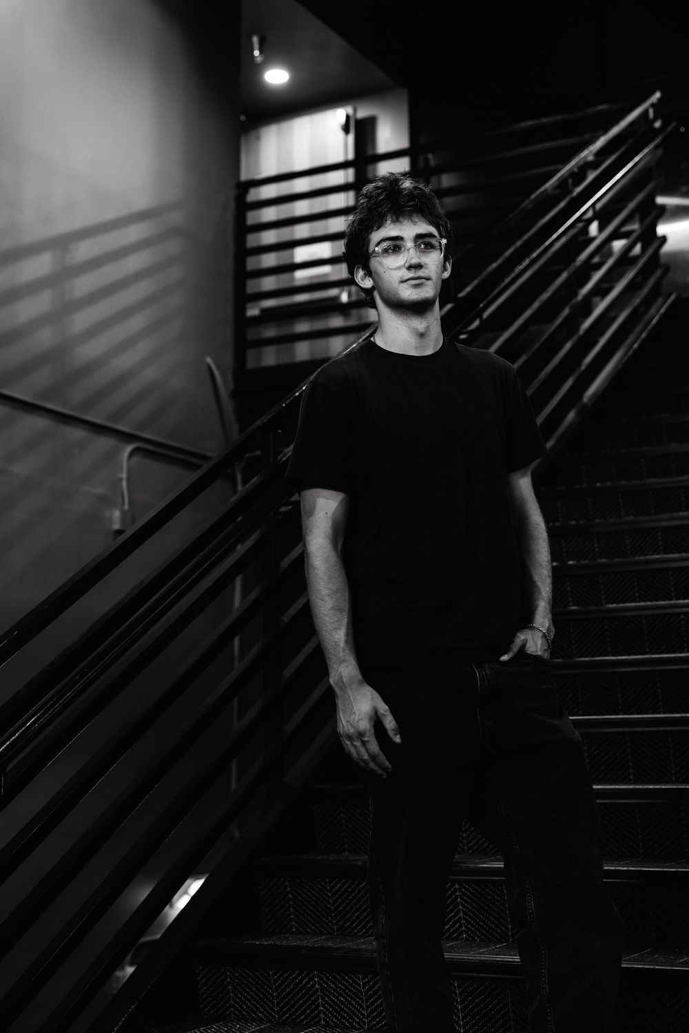 Young man in black t-shirt standing on dark staircase, black and white portrait photography.