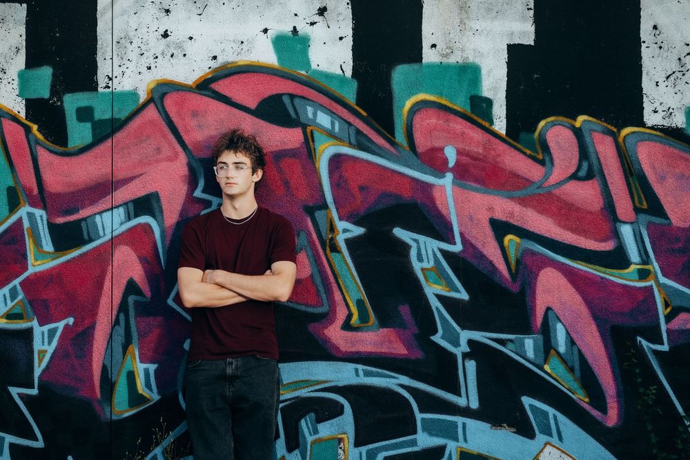 Young man with crossed arms posing confidently in front of vibrant colorful graffiti wall art.