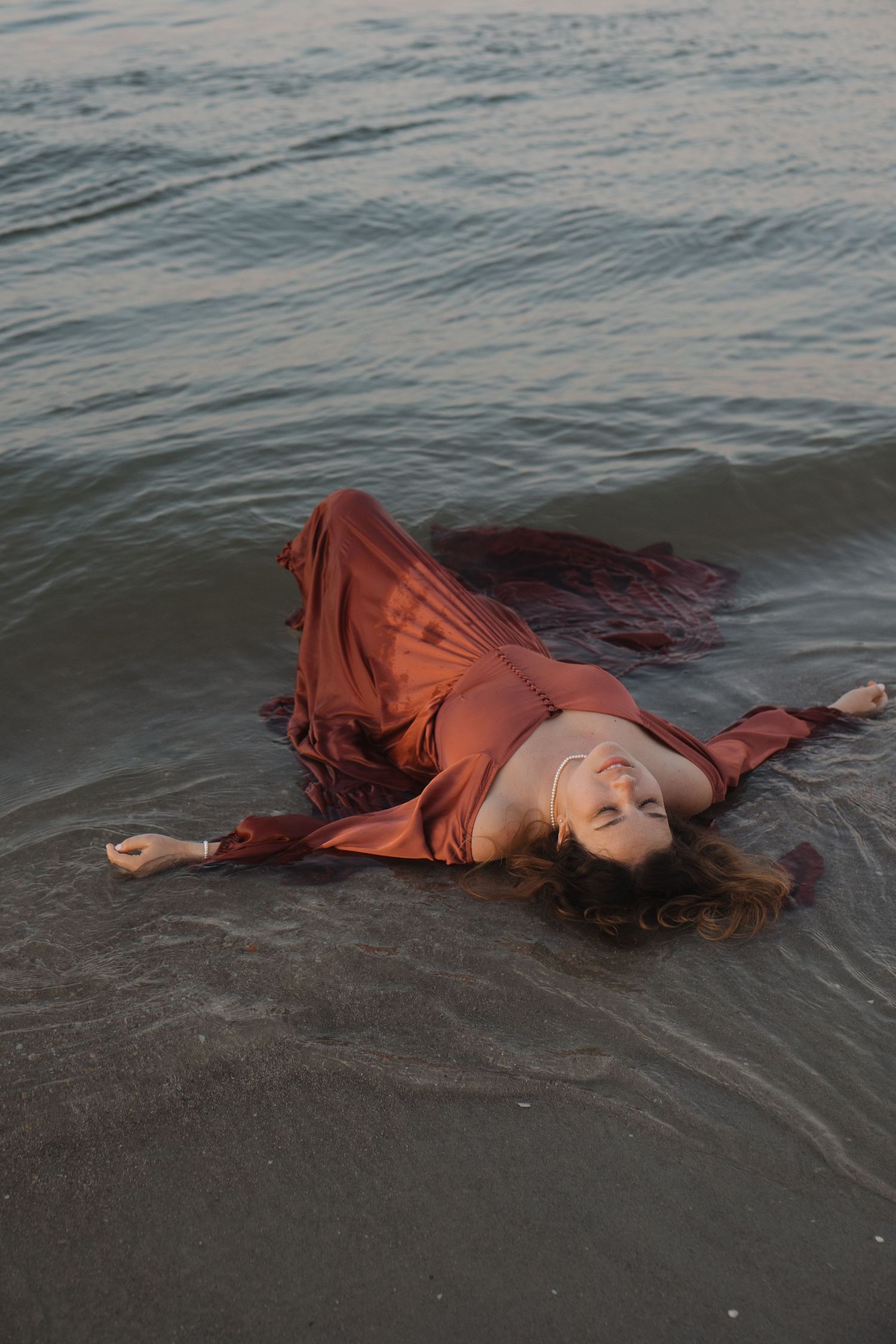 A woman in a rust colored dress laying in the water