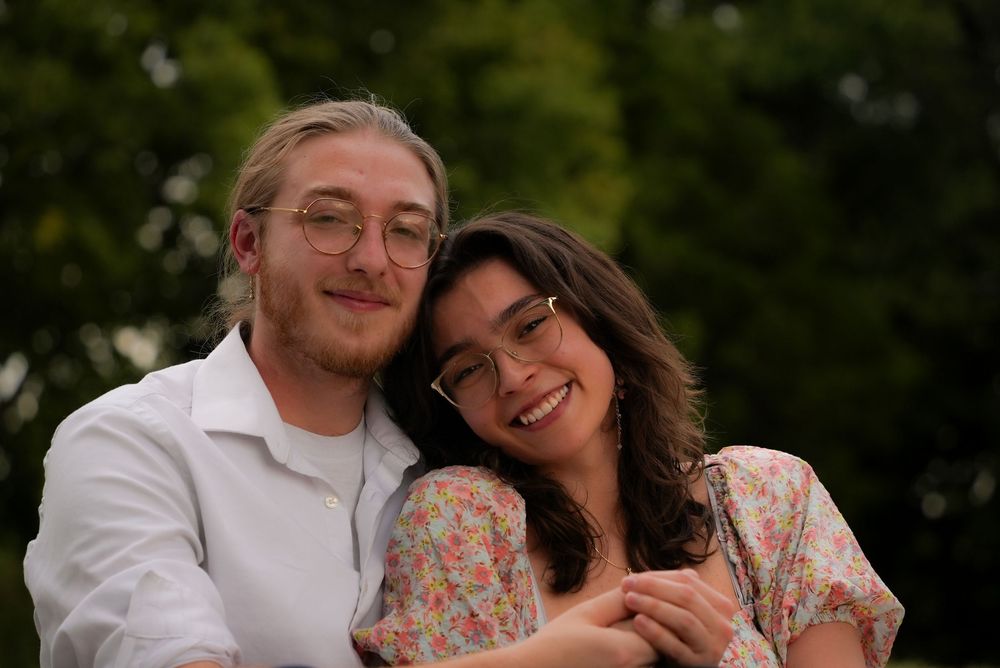 Young couple smiling and embracing outdoors in a lush green park setting.