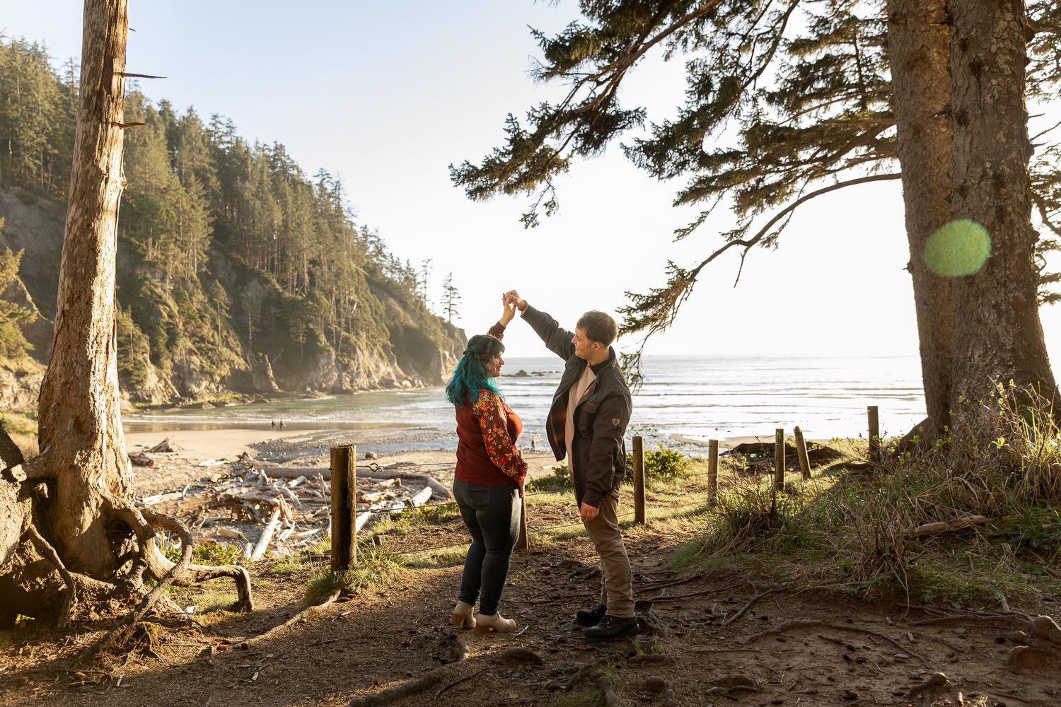 Couple dancing together on a scenic coastal trail surrounded by pine trees with ocean views in the background.