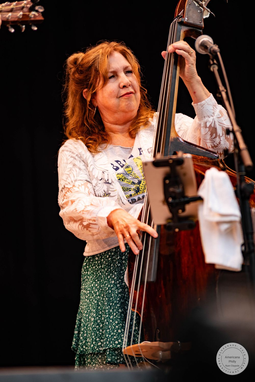 Woman playing upright bass on stage wearing a white floral top and green skirt during a live music performance.