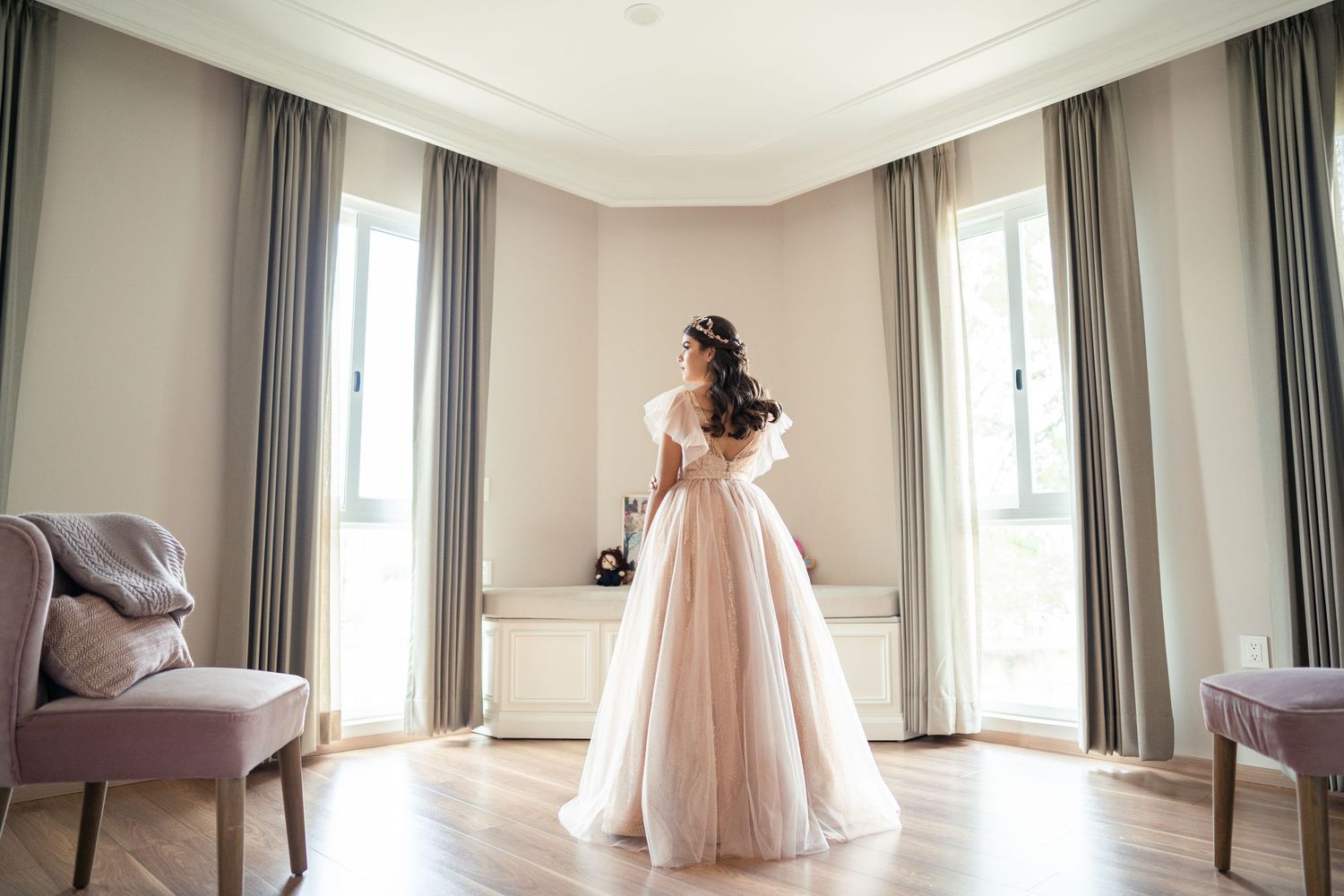 Una vista panorámica de una habitación luminosa con cortinas que llegan hasta el suelo y una persona con un vaporoso vestido rosa