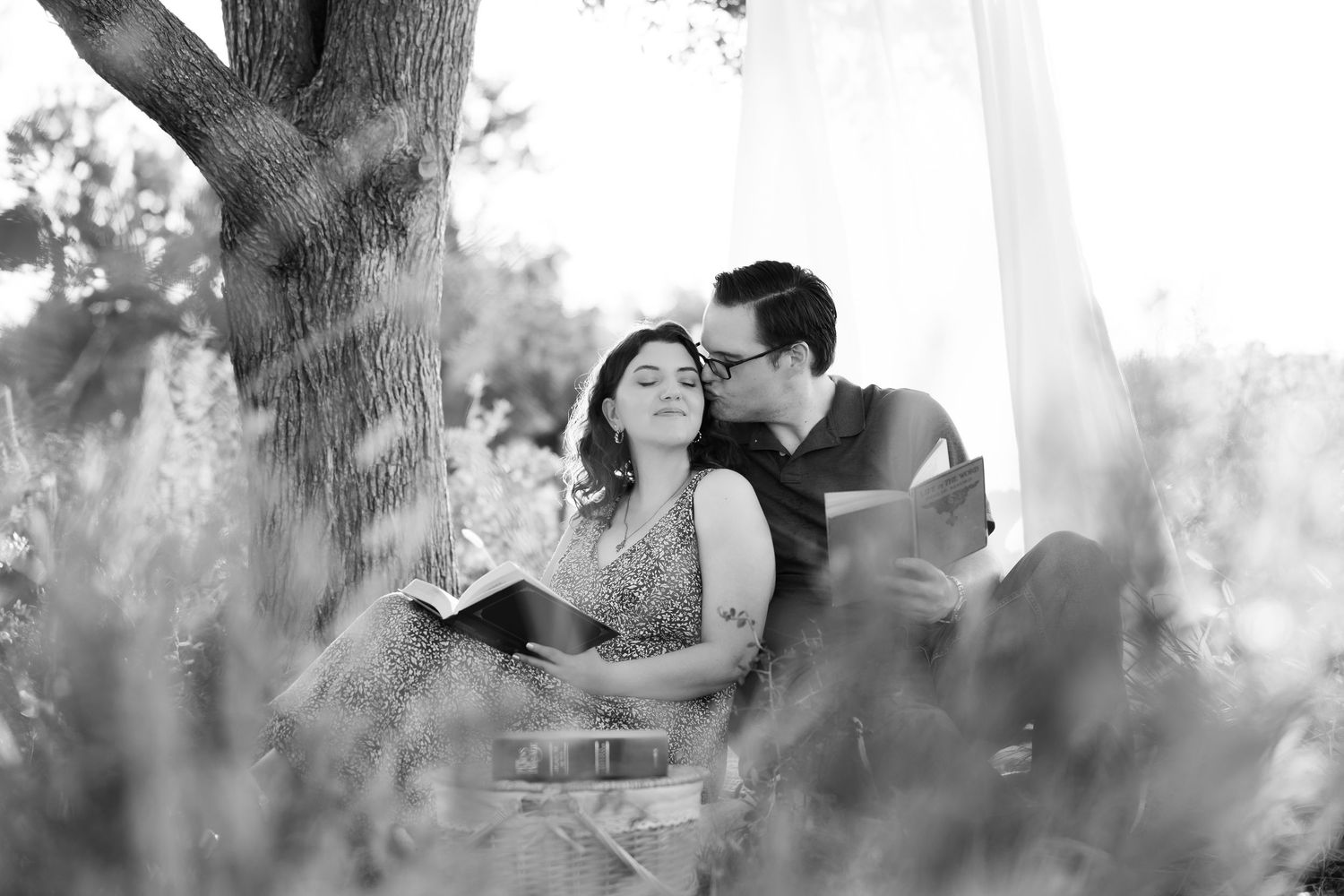 Black and white photo of happy young parents lying on a blanket outdoors with their smiling baby boy.