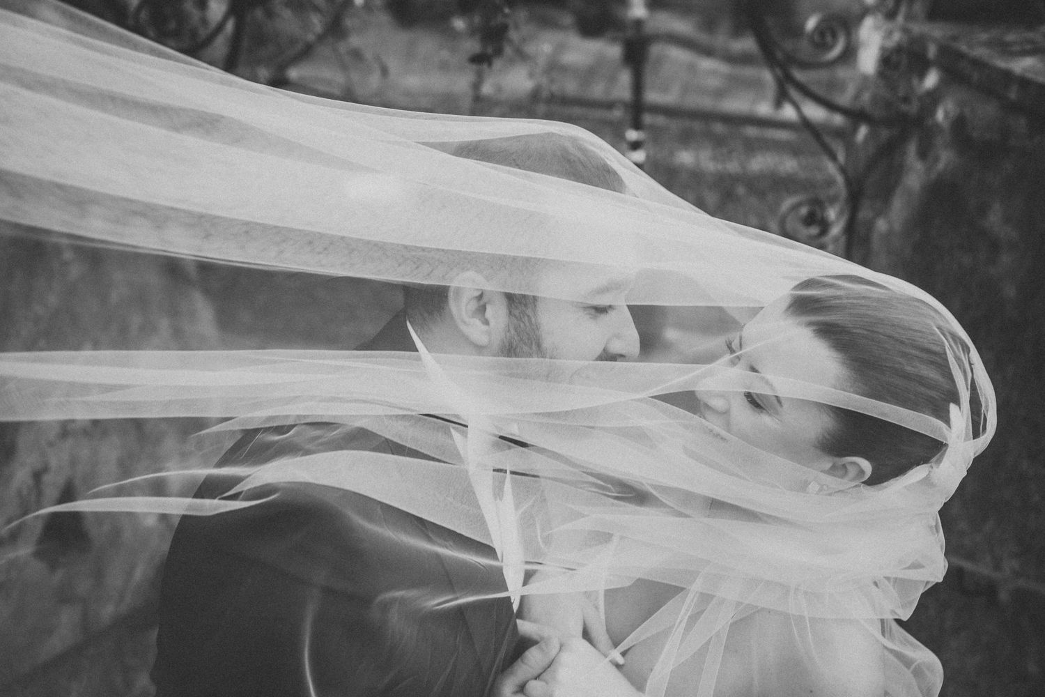Ethereal black and white portrait of a bride with windswept veil creating artistic lines.