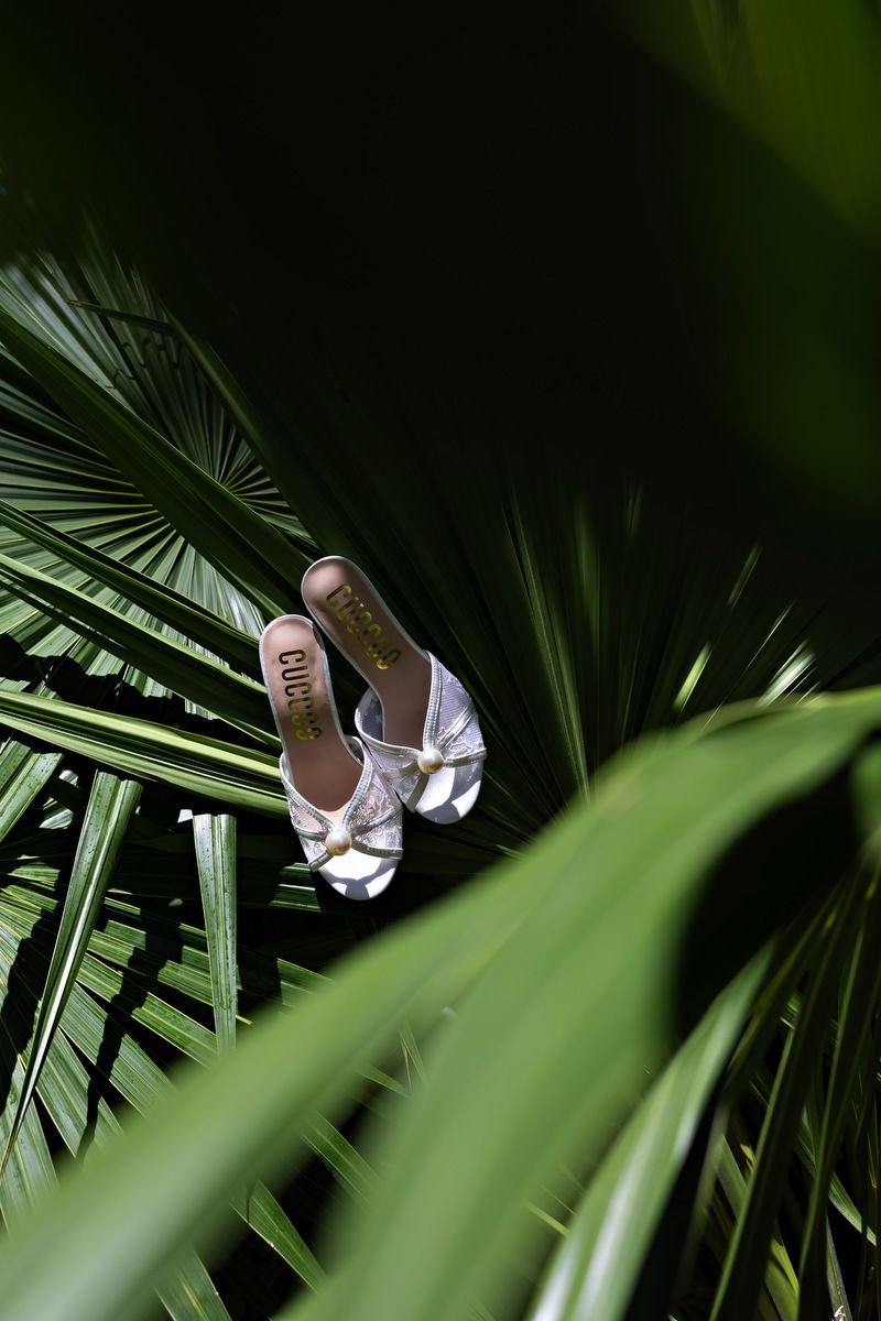 White bridal sandals displayed among lush tropical palm leaves in a creative flat lay photo.