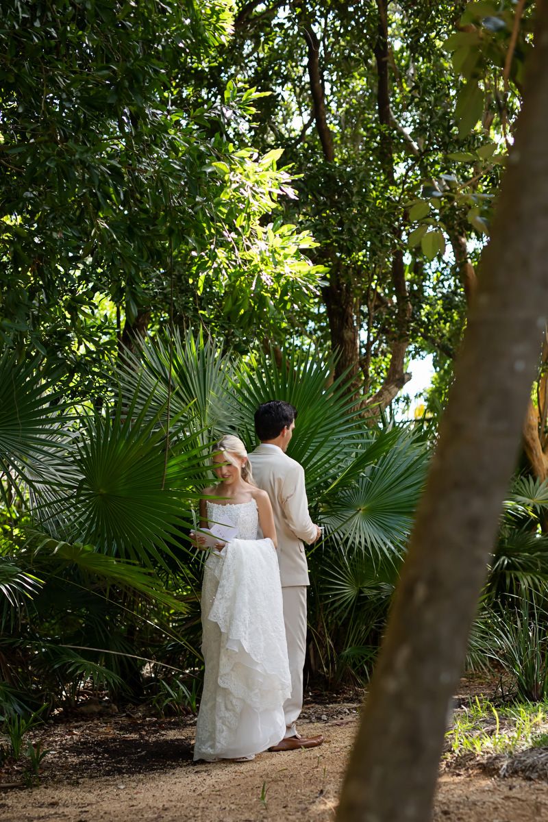 A bride and groom stand together on a garden path surrounded by lush tropical palm trees and greenery.