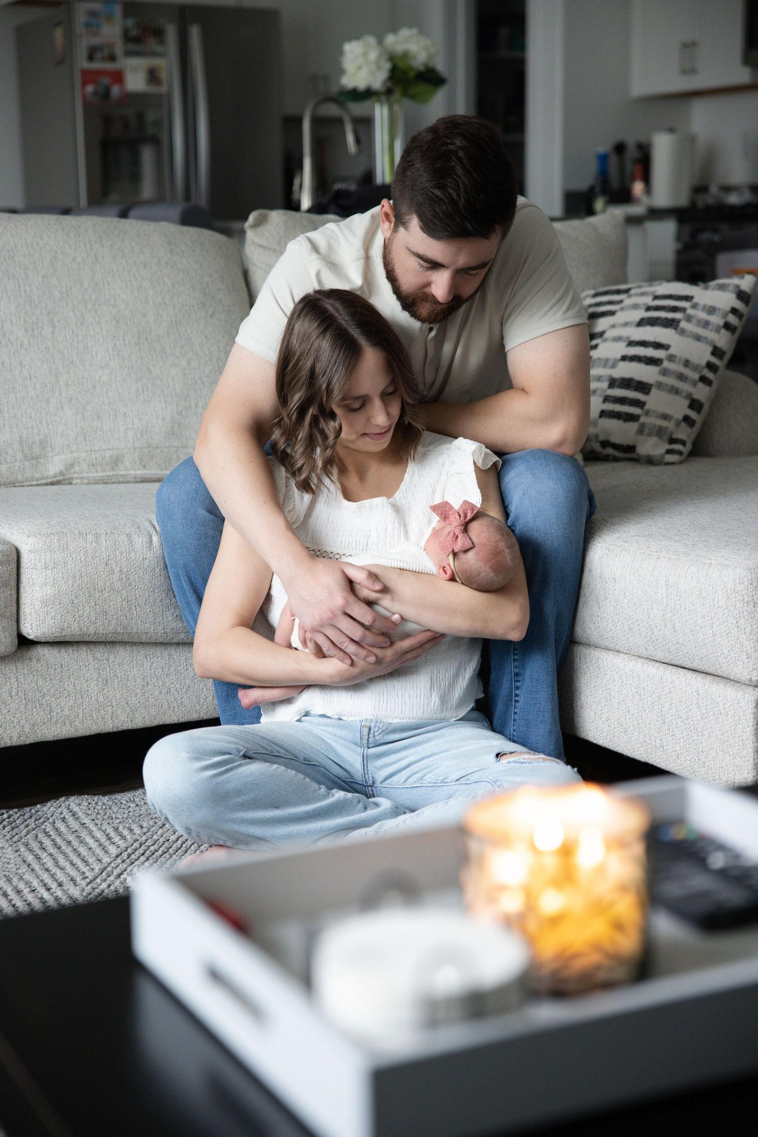 Parents cuddling their newborn beside a sofa during an in-home family portrait.