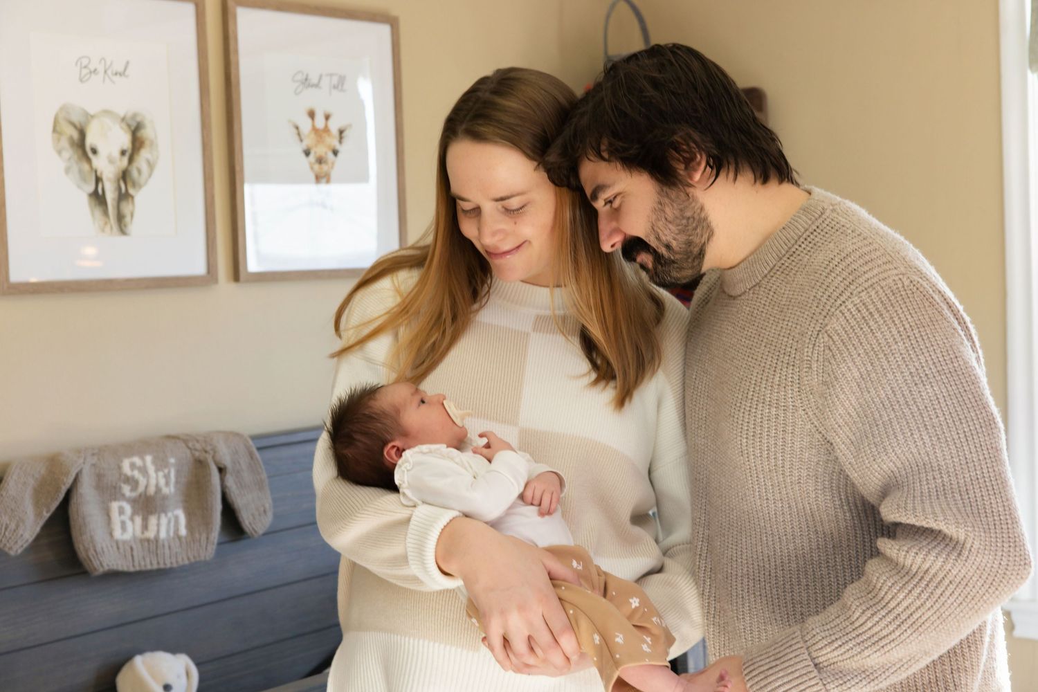 New parents lovingly gaze at their newborn baby in a cozy nursery with animal prints on the wall.