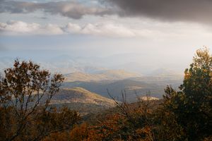Stunning autumn mountain valley landscape with dramatic clouds and colorful fall foliage in the foreground.
